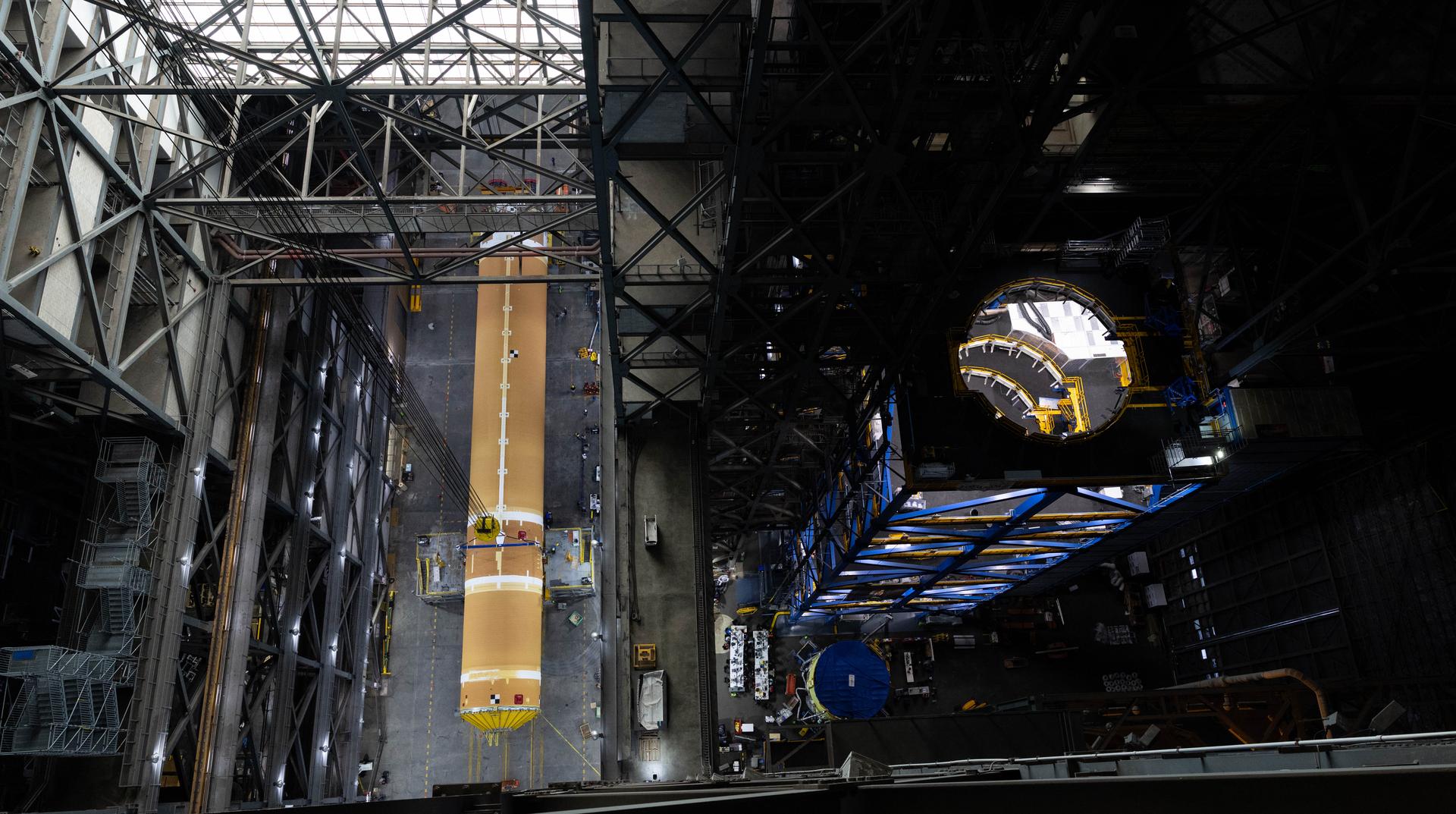 Vertical overhead view of a rocket stage extending through the center of a large assembly building, framed by surrounding platforms and structure.