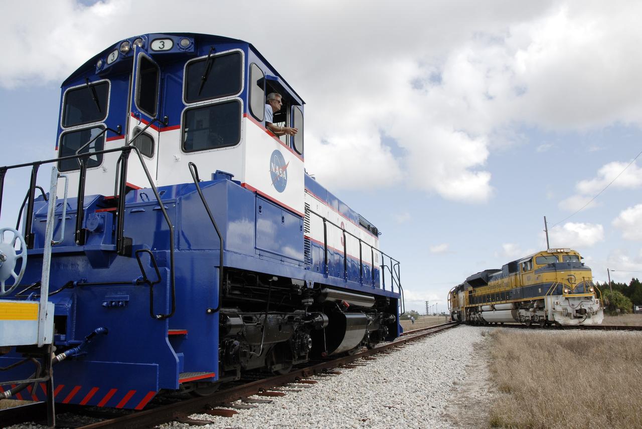 CAPE CANAVERAL, Fla. – The Florida East Coast Railway train arrives at the Jay Jay Rail Yard with the booster segments for the Ares I-X test rocket for interchange with the NASA Railroad (left).  The four reusable motor segments and the nozzle exit cone, manufactured by the Ares I first-stage prime contractor Alliant Techsystems Inc., or ATK, departed Utah March 12 on the seven-day, cross-country trip to Florida.  The segments will be delivered to the  Rotation, Processing and Surge Facility for final processing and integration. The booster used for the Ares I-X launch is being modified by adding new forward structures and a fifth segment simulator. The motor is the final hardware needed for the rocket's upcoming test flight this summer. The stacking operations are scheduled to begin in the Vehicle Assembly Building in April.   Photo credit: NASA/Kim Shiflett