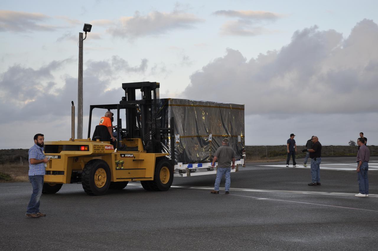 Workers push the pallet supporting the transportation container protecting NASA's Soil Moisture Active Passive, or SMAP, spacecraft into the Astrotech payload processing facility on Vandenberg Air Force Base in California. SMAP will launch on a Delta II 7320 configuration vehicle featuring a United Launch Alliance first stage booster powered by an Aerojet Rocketdyne RS-27A main engine and three Alliant Techsystems, or ATK, strap-on solid rocket motors. Once on station in Earth orbit, SMAP will provide global measurements of soil moisture and its freeze/thaw state. These measurements will be used to enhance understanding of processes that link the water, energy and carbon cycles, and to extend the capabilities of weather and climate prediction models. SMAP data also will be used to quantify net carbon flux in boreal landscapes and to develop improved flood prediction and drought monitoring capabilities. Launch from Space Launch Complex 2 is targeted for Jan. 29, 2015. 