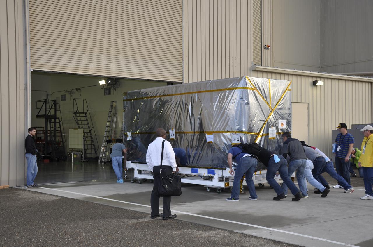 Workers push the pallet supporting the transportation container protecting NASA's Soil Moisture Active Passive, or SMAP, spacecraft into the Astrotech payload processing facility on Vandenberg Air Force Base in California. SMAP will launch on a Delta II 7320 configuration vehicle featuring a United Launch Alliance first stage booster powered by an Aerojet Rocketdyne RS-27A main engine and three Alliant Techsystems, or ATK, strap-on solid rocket motors. Once on station in Earth orbit, SMAP will provide global measurements of soil moisture and its freeze/thaw state. These measurements will be used to enhance understanding of processes that link the water, energy and carbon cycles, and to extend the capabilities of weather and climate prediction models. SMAP data also will be used to quantify net carbon flux in boreal landscapes and to develop improved flood prediction and drought monitoring capabilities. Launch from Space Launch Complex 2 is targeted for Jan. 29, 2015.