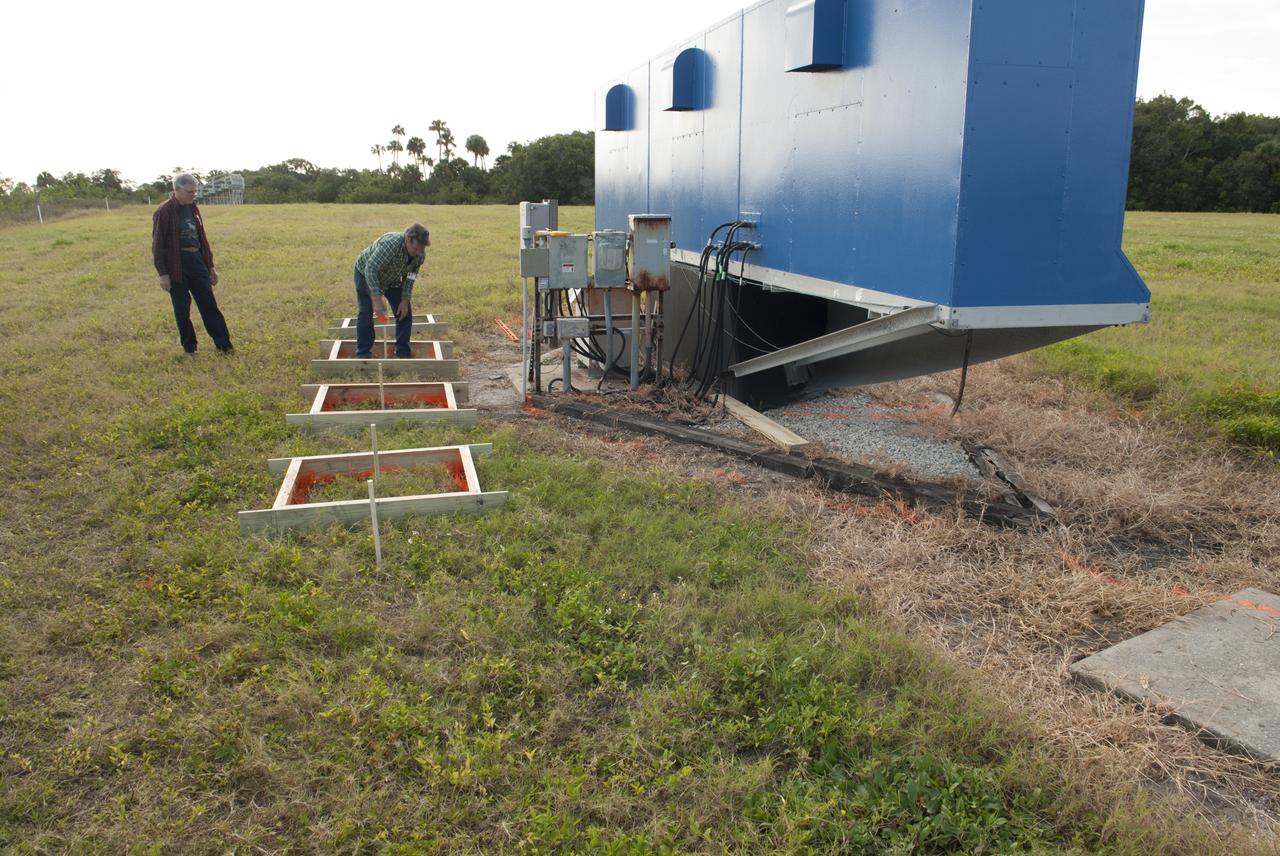 At NASA's Kennedy Space Center in Florida, Jeff Pratt and Frank Morse with Abacus Technology prep the area behind the current countdown clock for the groundbreaking ceremony for the new countdown clock. The old timepiece was designed by Kennedy engineers and built by Kennedy technicians in 1969. Not including the triangular concrete and aluminum base, the famous landmark is nearly 6 feet 70 inches high, 26 feet 315 inches wide and 3 feet deep. The new display will be similar in size, with the screen being nearly 26 feet wide by 7 feet high. 