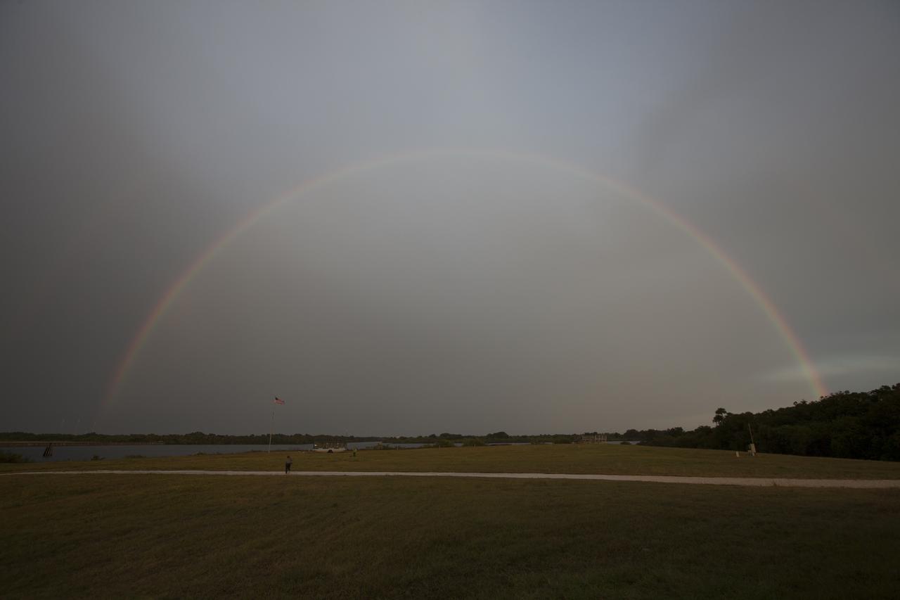 As rain showers dissipate, a rainbow appeared over the Kennedy Space Center's Press Site and turn basin. In the background is the historic countdown clock.