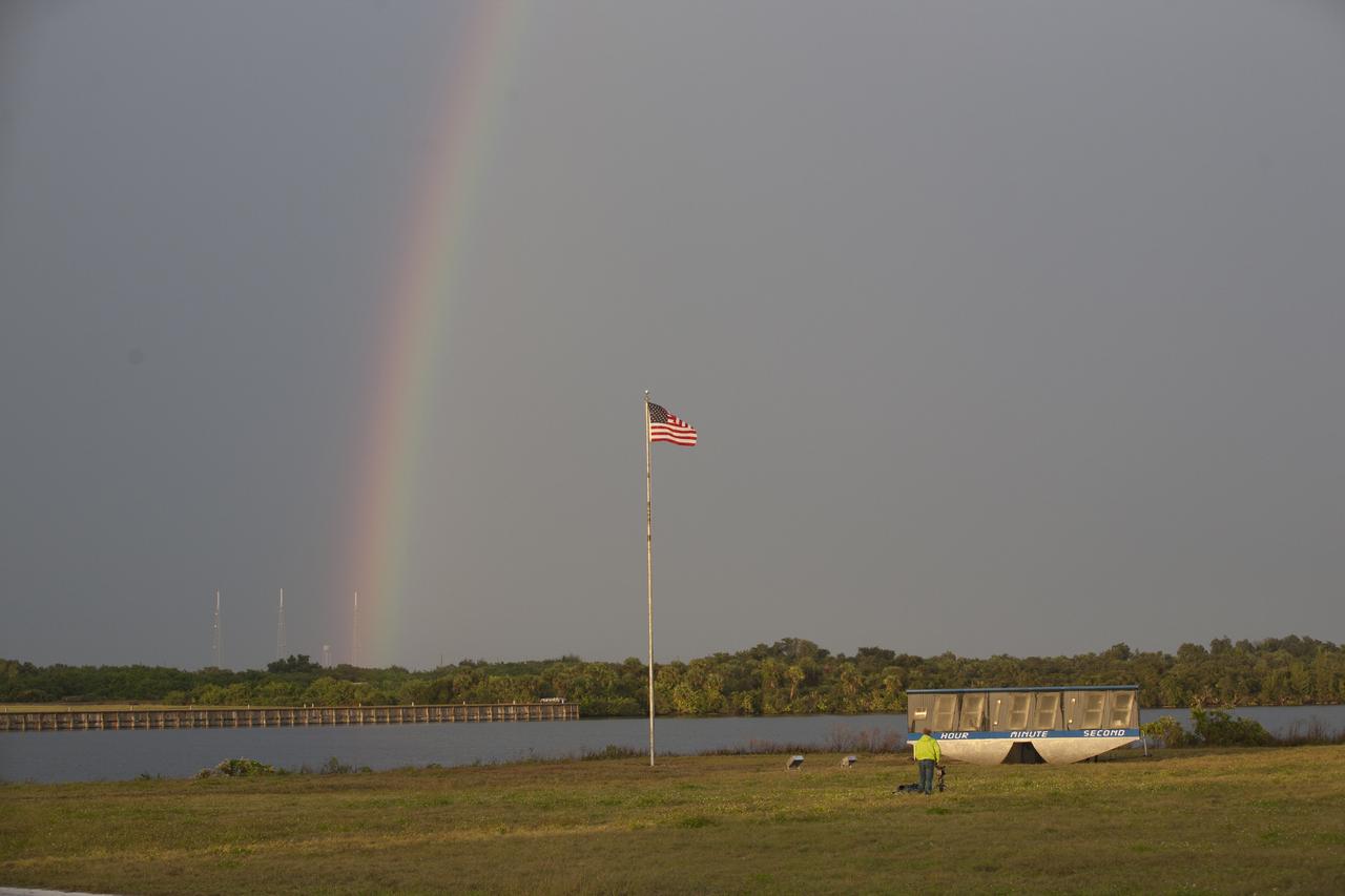 As rain showers dissipate, a rainbow appeared over the Kennedy Space Center's Press Site and turn basin. In the foreground is the historic countdown clock. In the background, is Launch Pad 39B where agency's Space Launch System will launch astronauts aboard the Orion spacecraft to deep-space destinations such as an asteroid and Mars. 