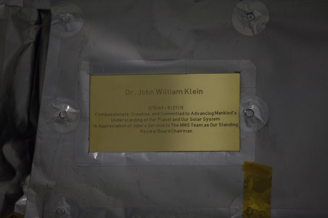 A plaque affixed to the side of a Magnetospheric Multiscale, or MMS, observatory dedicates the mission to Dr. John William Klein, now deceased, who served the MMS team as the standing review board chairman. MMS, led by a team from NASA's Goddard Space Flight Center, is a Solar Terrestrial Probes mission consisting of four identically instrumented spacecraft that will use Earth’s magnetosphere as a laboratory to study the microphysics of three fundamental plasma processes: magnetic reconnection, energetic particle acceleration and turbulence. Launch aboard a United Launch Alliance Atlas V rocket from Space Launch Complex 41 on Cape Canaveral Air Force Station is targeted for March 12, 2015. 
