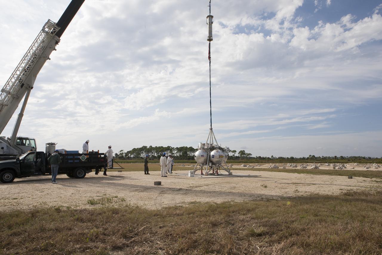 NASA's Project Morpheus prototype lander is prepared for lifting by a crane in preparation for a tethered-flight test at the north end of the Shuttle Landing Facility at NASA’s Kennedy Space Center in Florida. For the 40-second test, the lander will be hoisted 20 feet. The spacecraft will ascend an additional five feet and hover for five seconds. Morpheus then will perform a 5.6-foot ascent coupled with a 9.8-foot traverse, and hover for five more seconds before returning to the launch point. A number of changes have been made, primarily focused on autonomous landing and hazard avoidance technology ALHAT and moving the Doppler Lidar to the front of the forward liquid oxygen tank. The tether test was cut short due to Morpheus exceeding onboard abort rate limits. The vehicle was taken back to the hangar and data from the test is being studied. After review, managers will determine when a new test date will be set. The landing facility provides the lander with the kind of field necessary for realistic testing, complete with rocks, craters and hazards to avoid. Morpheus’ ALHAT payload allows it to navigate to clear landing sites amidst rocks, craters and other hazards during its descent.