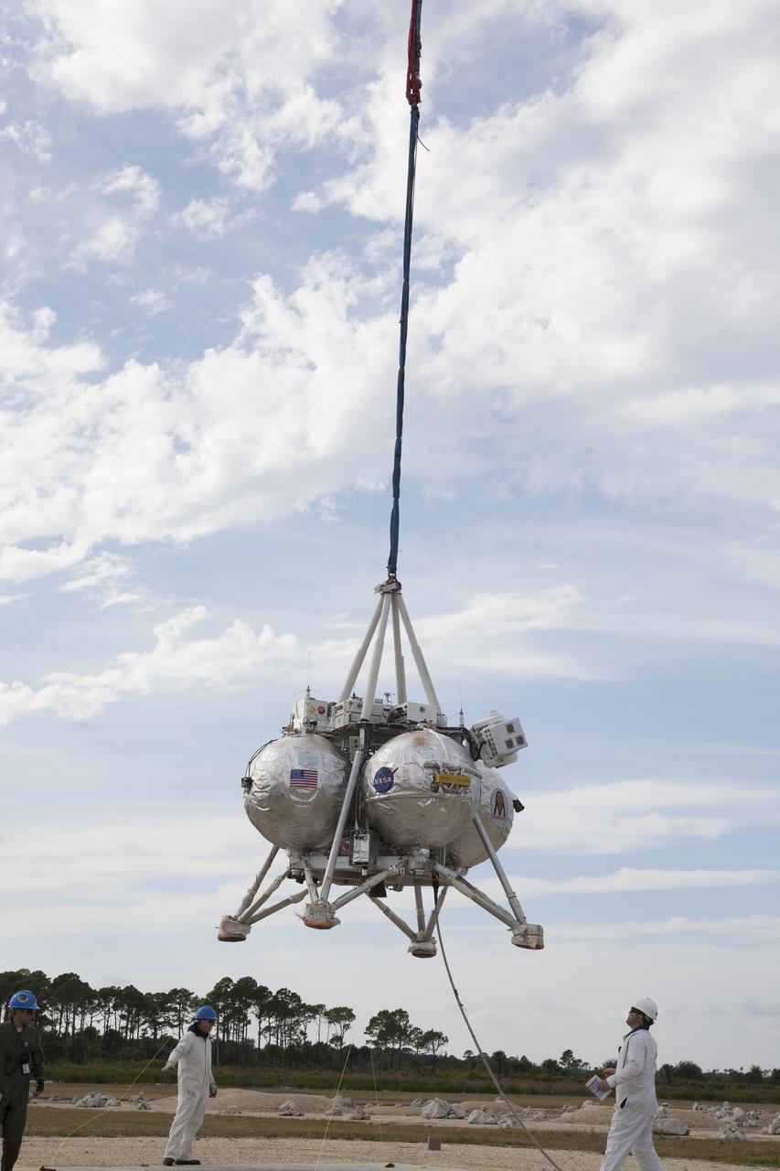 NASA's Project Morpheus prototype lander is lifted by a crane in preparation for a tethered-flight test at the north end of the Shuttle Landing Facility at NASA’s Kennedy Space Center in Florida. For the 40-second test, the lander will be hoisted 20 feet. The spacecraft will ascend an additional five feet and hover for five seconds. Morpheus then will perform a 5.6-foot ascent coupled with a 9.8-foot traverse, and hover for five more seconds before returning to the launch point. A number of changes have been made, primarily focused on autonomous landing and hazard avoidance technology ALHAT and moving the Doppler Lidar to the front of the forward liquid oxygen tank. The tether test was cut short due to Morpheus exceeding onboard abort rate limits. The vehicle was taken back to the hangar and data from the test is being studied. After review, managers will determine when a new test date will be set. The landing facility provides the lander with the kind of field necessary for realistic testing, complete with rocks, craters and hazards to avoid. Morpheus’ ALHAT payload allows it to navigate to clear landing sites amidst rocks, craters and other hazards during its descent.