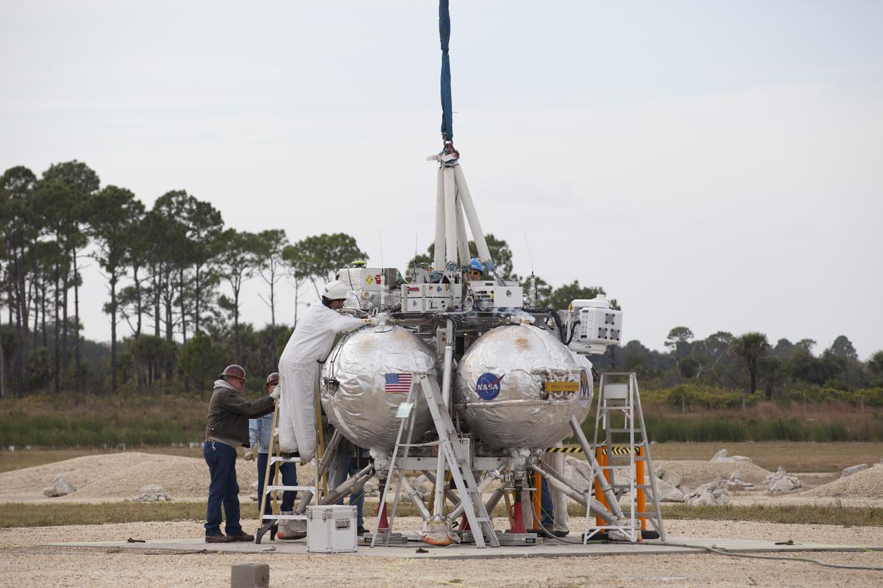 NASA's Project Morpheus prototype lander undergoes final preparations for a tethered-flight test at the north end of the Shuttle Landing Facility at NASA’s Kennedy Space Center in Florida. For the 40-second test, the lander will be hoisted 20 feet. The spacecraft will ascend an additional five feet and hover for five seconds. Morpheus then will perform a 5.6-foot ascent coupled with a 9.8-foot traverse, and hover for five more seconds before returning to the launch point. A number of changes have been made, primarily focused on autonomous landing and hazard avoidance technology ALHAT and moving the Doppler Lidar to the front of the forward liquid oxygen tank. The tether test was cut short due to Morpheus exceeding onboard abort rate limits. The vehicle was taken back to the hangar and data from the test is being studied. After review, managers will determine when a new test date will be set. The landing facility provides the lander with the kind of field necessary for realistic testing, complete with rocks, craters and hazards to avoid. Morpheus’ ALHAT payload allows it to navigate to clear landing sites amidst rocks, craters and other hazards during its descent.