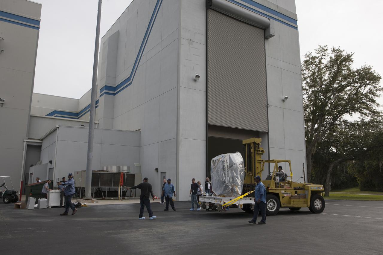 NOAA’s Deep Space Climate Observatory spacecraft, or DSCOVR, wrapped in plastic and secured onto a portable work stand, makes a short trek from the airlock of Building 2 to the high bay of Building 1 at the Astrotech payload processing facility.