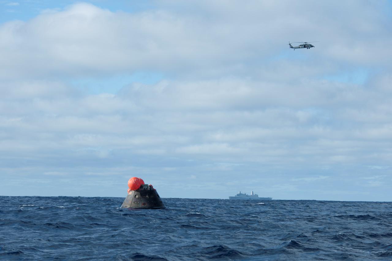 NASA's Orion spacecraft floats in the Pacific Ocean after splashdown from its first flight test in Earth orbit. An H60-S Seahawk helicopter hovers above to communicate the spacecraft's location back to the USS Anchorage, in the distance. NASA, the U.S. Navy and Lockheed Martin are coordinating efforts to recover Orion and secure the spacecraft in the well deck of the USS Anchorage. Orion completed a two-orbit, four-and-a-half hour mission, to test systems critical to crew safety, including the launch abort system, the heat shield and the parachute system. The Ground Systems Development and Operations Program is leading the recovery efforts.