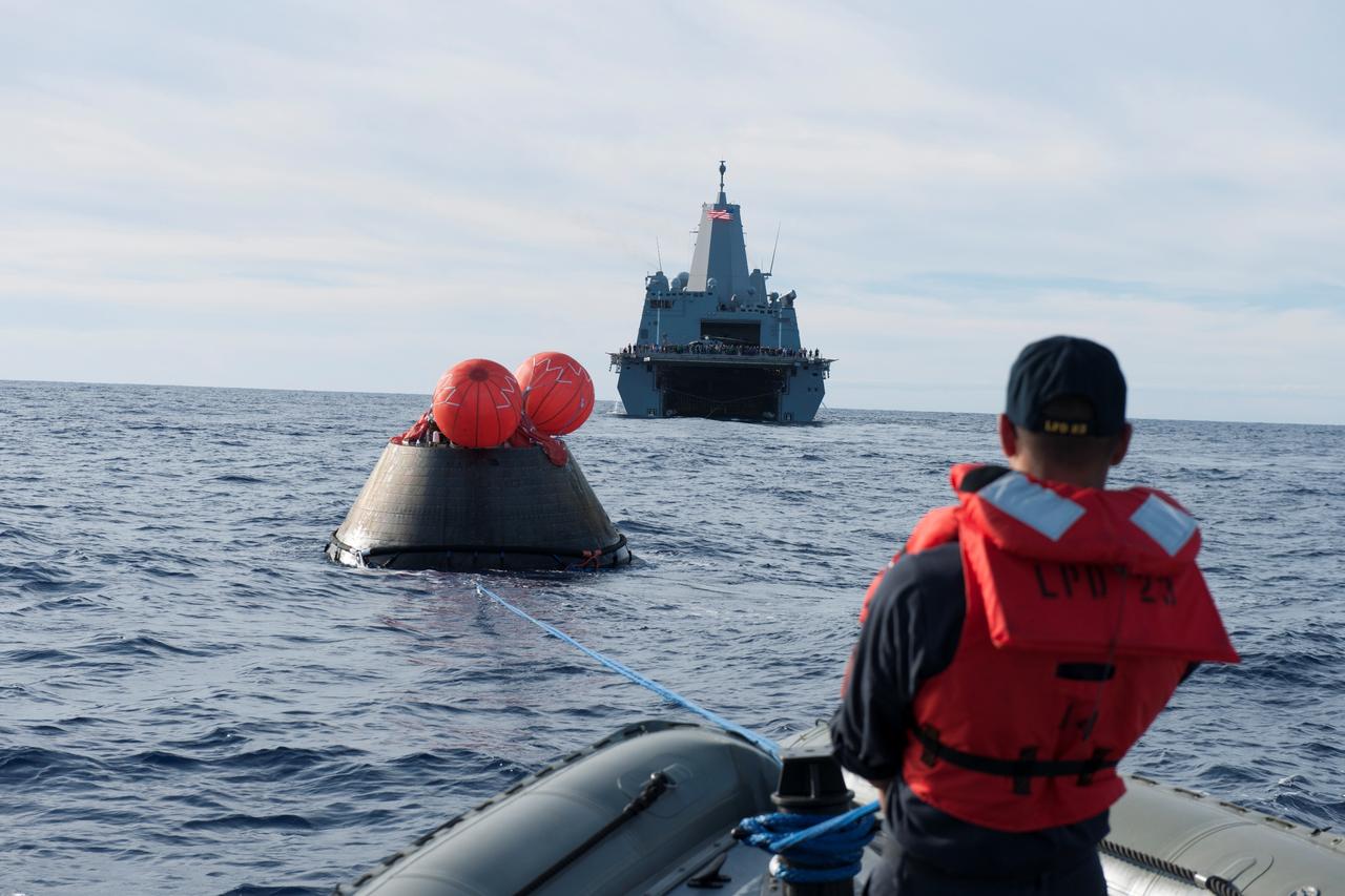 U.S. Navy personnel aboard a rigid hull inflatable boat help recover NASA's Orion spacecraft following its splashdown in the Pacific Ocean after its first flight test in Earth orbit. The USS Anchorage is in the background. NASA, the U.S. Navy and Lockheed Martin are coordinating efforts to recover Orion and secure the spacecraft in the well deck of the USS Anchorage. Orion completed a two-orbit, four-and-a-half hour mission, to test systems critical to crew safety, including the launch abort system, the heat shield and the parachute system. The Ground Systems Development and Operations Program is leading the recovery efforts.