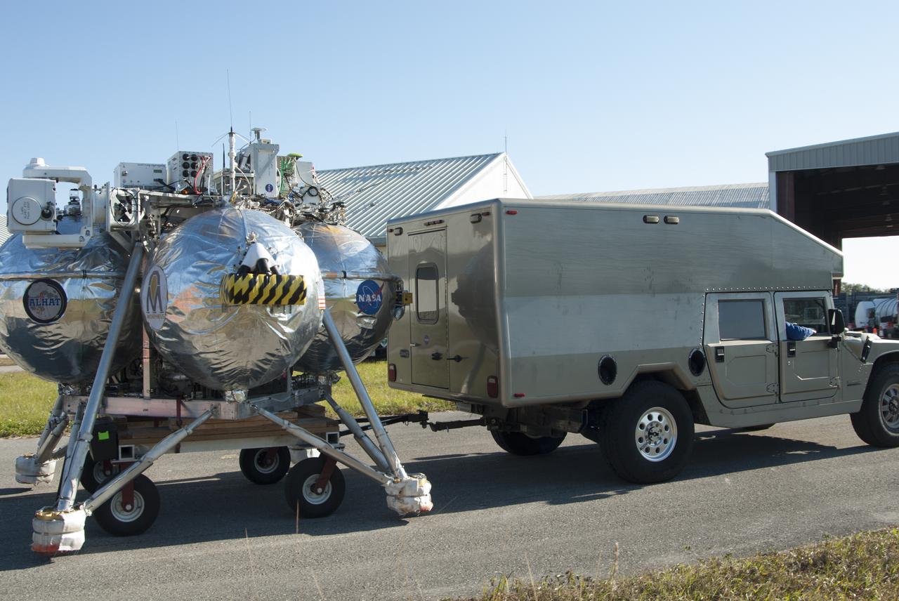 NASA's Project Morpheus prototype lander is being transported from a hangar at the Shuttle Landing Facility, or SLF, for free flight test number 15 at the north end of the SLF at NASA’s Kennedy Space Center in Florida. The lander will take off from the ground over a flame trench and use its autonomous landing and hazard avoidance technology, or ALHAT sensors, to survey the hazard field to determine safe landing sites. Project Morpheus tests NASA’s ALHAT and an engine that runs on liquid oxygen and methane, which are green propellants. These new capabilities could be used in future efforts to deliver cargo to planetary surfaces. Project Morpheus is being managed under the Advanced Exploration Systems, or AES, Division in NASA’s Human Exploration and Operations Mission Directorate. 