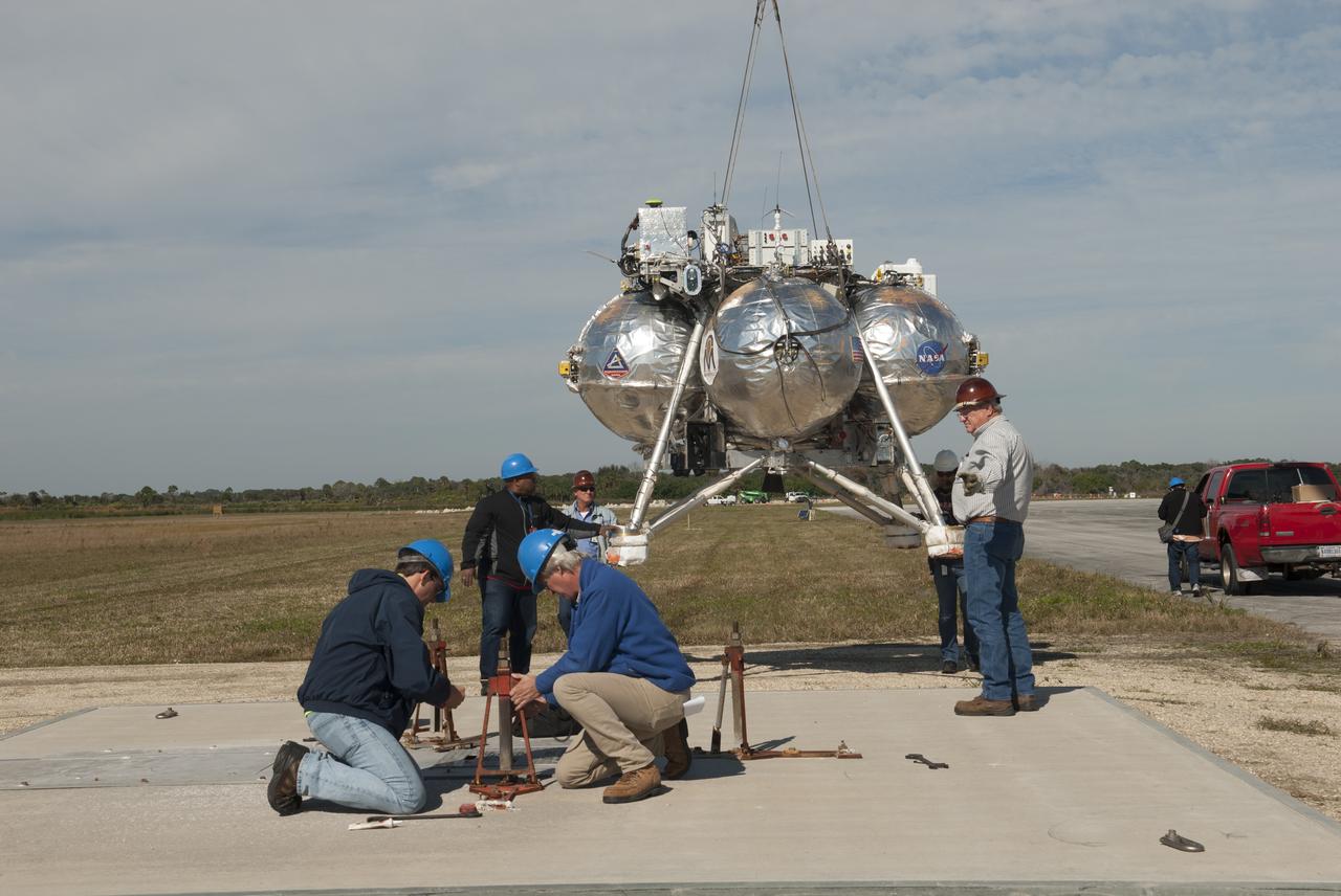 Engineers and technicians prepare the launch pad for NASA's Project Morpheus prototype lander at the north end of the Shuttle Landing Facility at NASA's Kennedy Space Center in Florida. Morpheus is being prepared for free flight test number 15 at the SLF. The lander will take off from the ground over a flame trench and use its autonomous landing and hazard avoidance technology, or ALHAT sensors, to survey the hazard field to determine safe landing sites. Project Morpheus tests NASA’s ALHAT and an engine that runs on liquid oxygen and methane, which are green propellants. These new capabilities could be used in future efforts to deliver cargo to planetary surfaces. Project Morpheus is being managed under the Advanced Exploration Systems, or AES, Division in NASA’s Human Exploration and Operations Mission Directorate. 