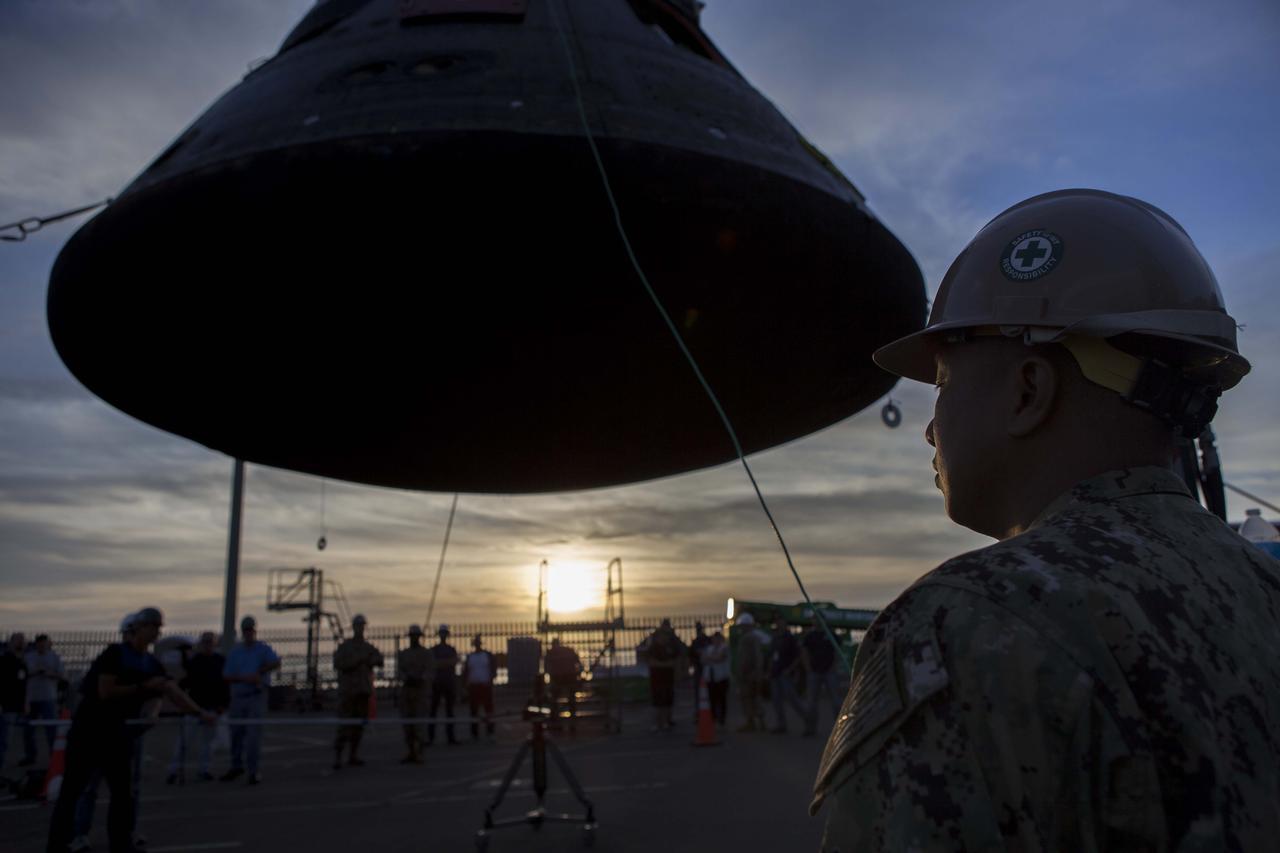 Just before sunset, the Orion crew module is being moved by crane from its crew module recovery cradle and will be placed in the crew module transportation fixture at the Mole Pier at Naval Base San Diego in California. The fixture has been secured on the back of a flatbed truck. Orion is being prepared for the overland trip back to NASA's Kennedy Space Center in Florida. Orion was recovered from the Pacific Ocean after completing a two-orbit, four-and-a-half hour mission Dec. 5 to test systems critical to crew safety, including the launch abort system, the heat shield and the parachute system. NASA, the U.S. Navy and Lockheed Martin coordinated efforts to recover Orion. The Ground Systems Development and Operations Program led the recovery, offload and pre-transportation efforts. 