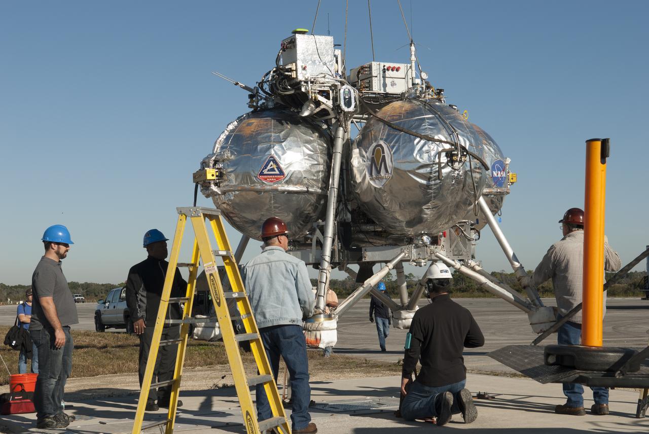 Engineers and technicians prepare NASA's Project Morpheus prototype lander for free flight test No. 15 at the north end of the Shuttle Landing Facility at Kennedy Space Center in Florida. During the 97-second test, onboard autonomous landing and hazard avoidance technology sensors, or ALHAT, surveyed the hazard field for safe landing sites, then guided the lander forward and downward to a successful landing.