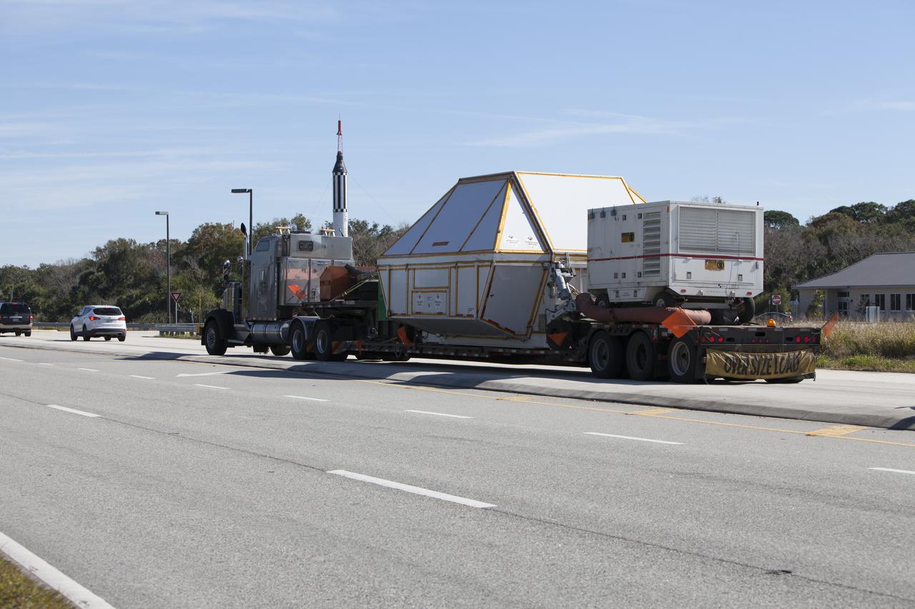 NASA's Orion crew module, enclosed in its crew module transportation fixture and secured on a flatbed truck nears the entrance gate to Kennedy Space Center in Florida. In the background is a full-scale mockup of the Mercury Redstone rocket that boosted NASA astronauts Alan Shepard and Virgil "Gus" Grissom on their 1961 sub-orbital missions that began America's human spaceflight program. Orion made the overland trip from Naval Base San Diego in California. Orion was recovered from the Pacific Ocean after completing a two-orbit, four-and-a-half hour mission Dec. 5 to test systems critical to crew safety, including the launch abort system, the heat shield and the parachute system. The Ground Systems Development and Operations Program led the recovery, offload and transportation efforts.