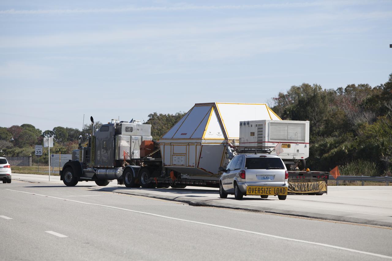 NASA's Orion crew module, enclosed in its crew module transportation fixture and secured on a flatbed truck nears the entrance gate to Kennedy Space Center in Florida. Orion made the overland trip from Naval Base San Diego in California. Orion was recovered from the Pacific Ocean after completing a two-orbit, four-and-a-half hour mission Dec. 5 to test systems critical to crew safety, including the launch abort system, the heat shield and the parachute system. The Ground Systems Development and Operations Program led the recovery, offload and transportation efforts.
