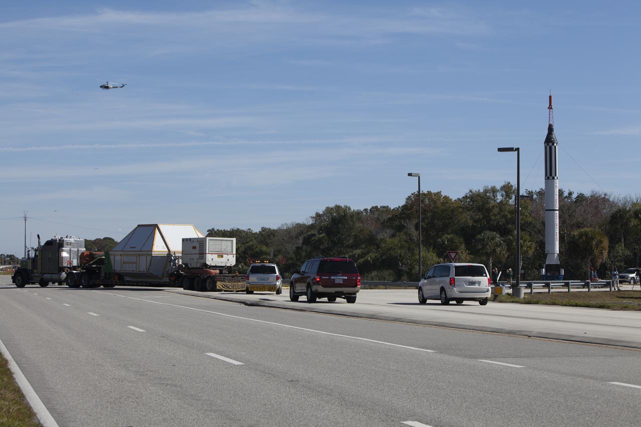 NASA's Orion crew module, enclosed in its crew module transportation fixture and secured on a flatbed truck nears the entrance gate to Kennedy Space Center in Florida. In the background is a full-scale mockup of the Mercury Redstone rocket that boosted NASA astronauts Alan Shepard and Virgil "Gus" Grissom on their 1961 sub-orbital missions that began America's human spaceflight program. Orion made the overland trip from Naval Base San Diego in California. Orion was recovered from the Pacific Ocean after completing a two-orbit, four-and-a-half hour mission Dec. 5 to test systems critical to crew safety, including the launch abort system, the heat shield and the parachute system. The Ground Systems Development and Operations Program led the recovery, offload and transportation efforts.