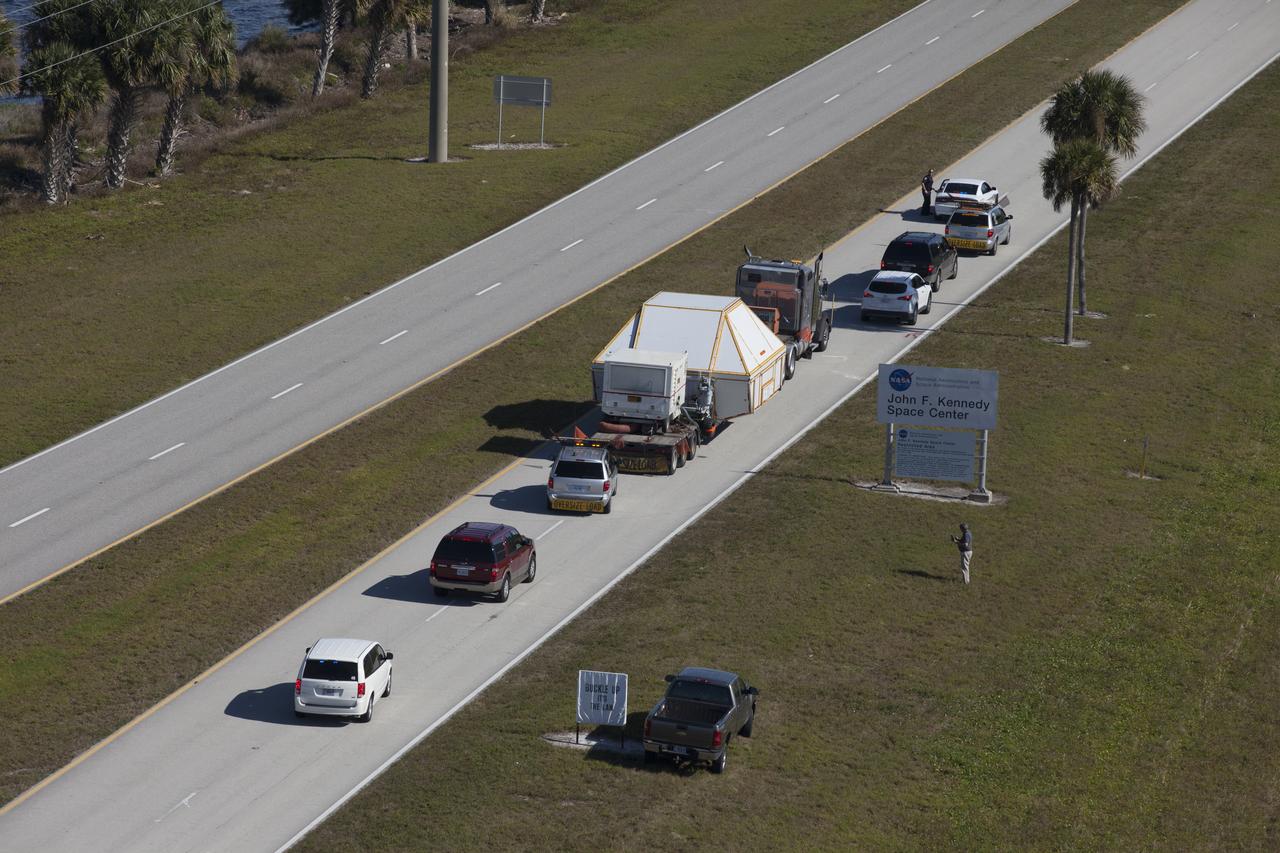 An aerial view near NASA's Kennedy Space Center Visitor Complex reveals the Orion crew module, enclosed in its crew module transportation fixture and secured on a flatbed truck on the NASA Causeway that leads to the entrance gate to Kennedy Space Center in Florida. Orion made the 2,700 mile overland trip from Naval Base San Diego in California. The spacecraft was recovered from the Pacific Ocean after completing a two-orbit, four-and-a-half hour mission Dec. 5 to test systems critical to crew safety, including the launch abort system, the heat shield and the parachute system. The Ground Systems Development and Operations Program led the recovery, offload and transportation efforts.