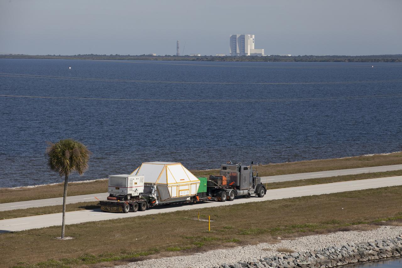 An aerial view near NASA's Kennedy Space Center Visitor Complex reveals the Orion crew module, enclosed in its crew module transportation fixture and secured on a flatbed truck that is proceeding along the NASA Causeway to the entrance gate to Kennedy Space Center in Florida. Across the inland waterway is the iconic Vehicle Assembly Building. Orion made the 2,700 mile overland trip from Naval Base San Diego in California. The spacecraft was recovered from the Pacific Ocean after completing a two-orbit, four-and-a-half hour mission Dec. 5 to test systems critical to crew safety, including the launch abort system, the heat shield and the parachute system. The Ground Systems Development and Operations Program led the recovery, offload and transportation efforts.