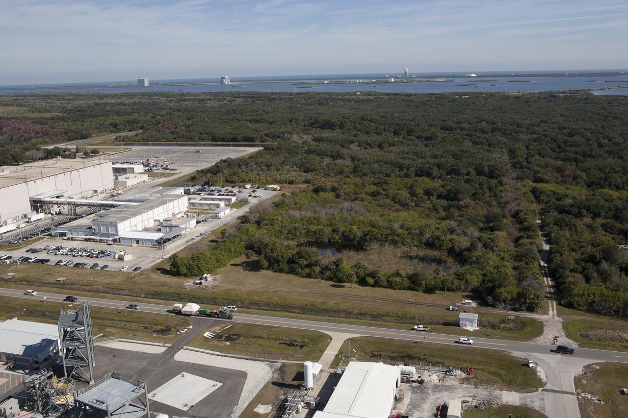 An aerial view reveals the Orion crew module, enclosed in its crew module transportation fixture and secured on a flatbed truck is passing the Space Station Processing Facility at Kennedy Space Center in Florida on its way to the Multi-Operation Support Building. Orion made the 2,700 mile overland trip from Naval Base San Diego in California. The spacecraft was recovered from the Pacific Ocean after completing a two-orbit, four-and-a-half hour mission Dec. 5 to test systems critical to crew safety, including the launch abort system, the heat shield and the parachute system. The Ground Systems Development and Operations Program led the recovery, offload and transportation efforts.