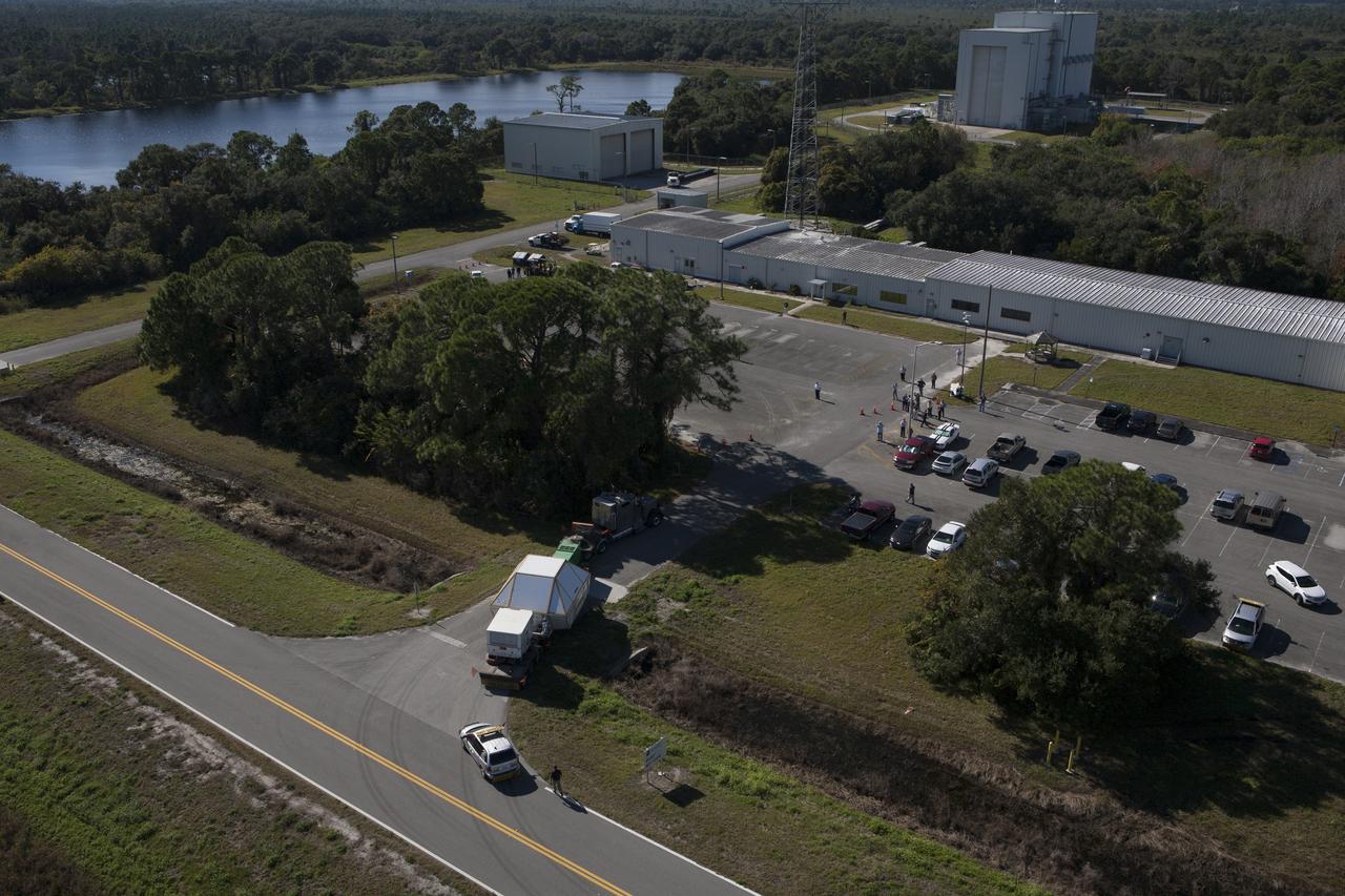 An aerial view reveals the Orion crew module, enclosed in its crew module transportation fixture and secured on a flatbed truck is proceeding to the Multi-Operation Support Building at NASA's Kennedy Space Center. Orion made the 2,700 mile overland trip from Naval Base San Diego in California. The spacecraft was recovered from the Pacific Ocean after completing a two-orbit, four-and-a-half hour mission Dec. 5 to test systems critical to crew safety, including the launch abort system, the heat shield and the parachute system. The Ground Systems Development and Operations Program led the recovery, offload and transportation efforts.
