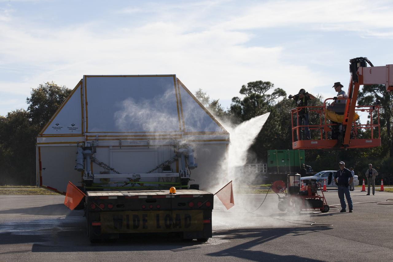 Technicians wash down the crew module transportation fixture containing the Orion crew module on the back of a flatbed truck at the Multi-Operation Support Building at NASA's Kennedy Space Center in Florida. Orion was transported 2,700 miles overland from Naval Base San Diego in California. Orion was recovered from the Pacific Ocean after completing a two-orbit, four-and-a-half hour mission Dec. 5 to test systems critical to crew safety, including the launch abort system, the heat shield and the parachute system. The Ground Systems Development and Operations Program led the recovery, offload and transportation efforts.