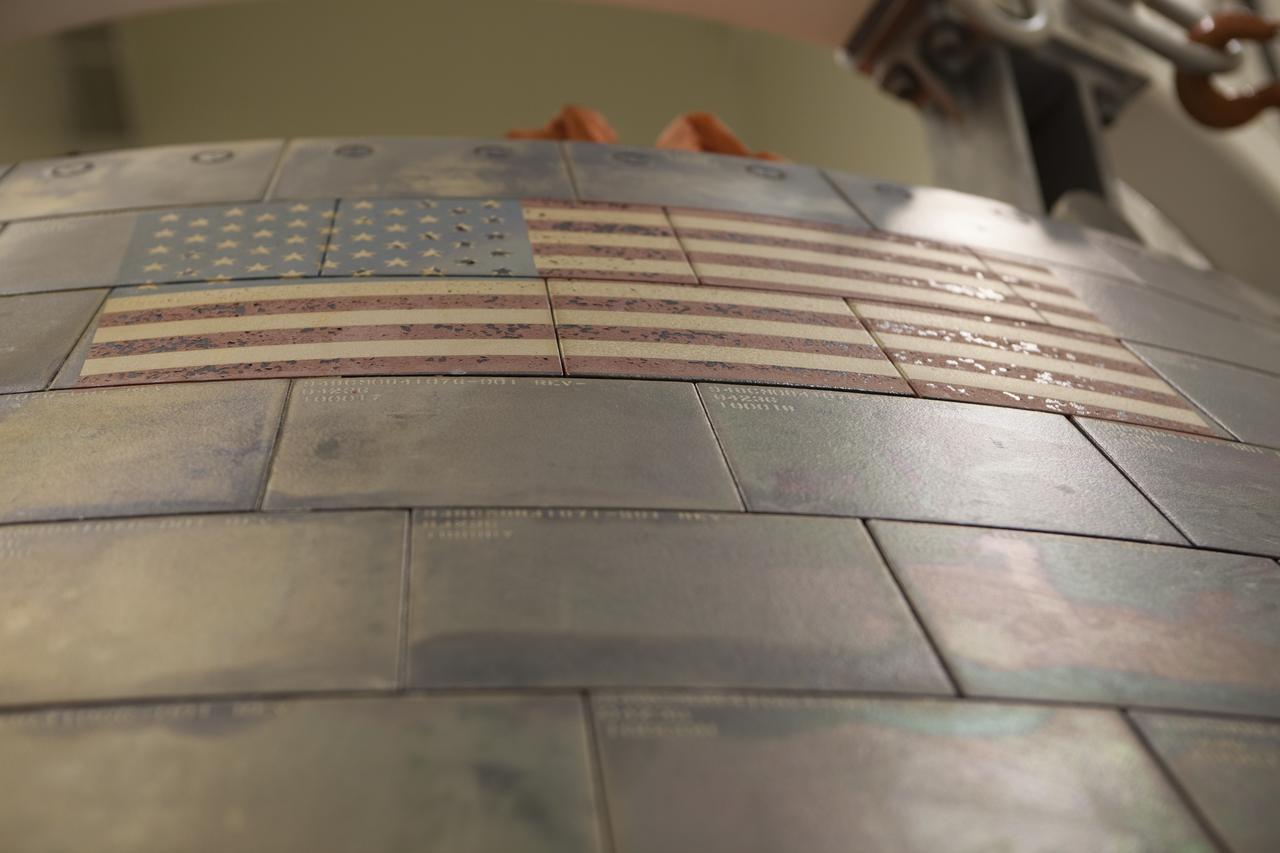 The U.S. Flag is in view on NASA's Orion spacecraft inside the Launch Abort System Facility at NASA's Kennedy Space Center in Florida during a media event. Orion made the 8-day, 2,700 mile overland trip back to Kennedy from Naval Base San Diego in California. Analysis of date obtained during its two-orbit, four-and-a-half hour mission Dec. 5 will provide engineers with detailed information on how the spacecraft fared. The Ground Systems Development and Operations Program led the recovery, offload and transportation efforts.