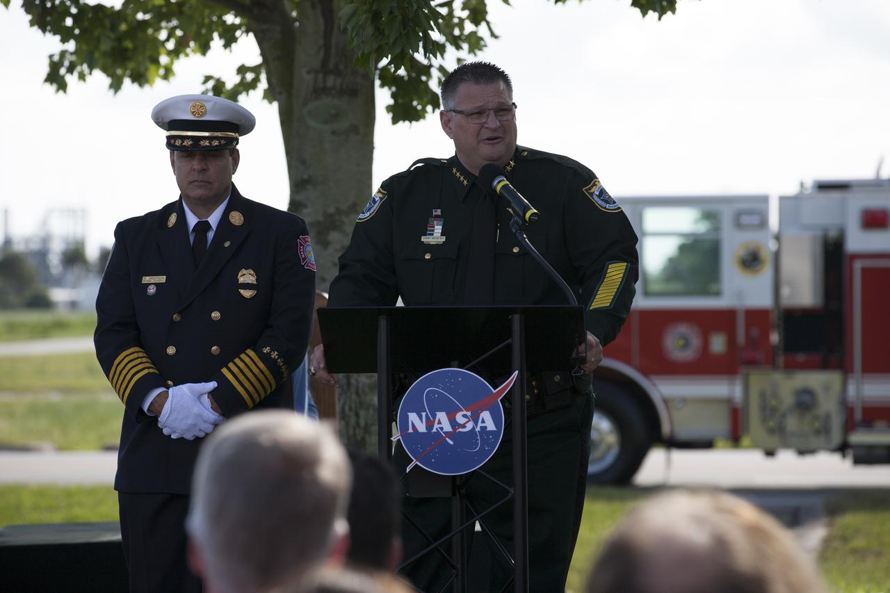 Rick Anderson, fire chief at NASA's Kennedy Space Center, on podium, left, and Brevard County Sheriff Wayne Ivey take part in the dedication service for a memorial to the 343 first responder victims of the Sept. 11, 2001, terror attacks at Kennedy's Fire Station 1 on Sept. 11, 2015. The ceremony dedicated a monument that includes a section of steel I-beam from the World Trade Center in New York. 