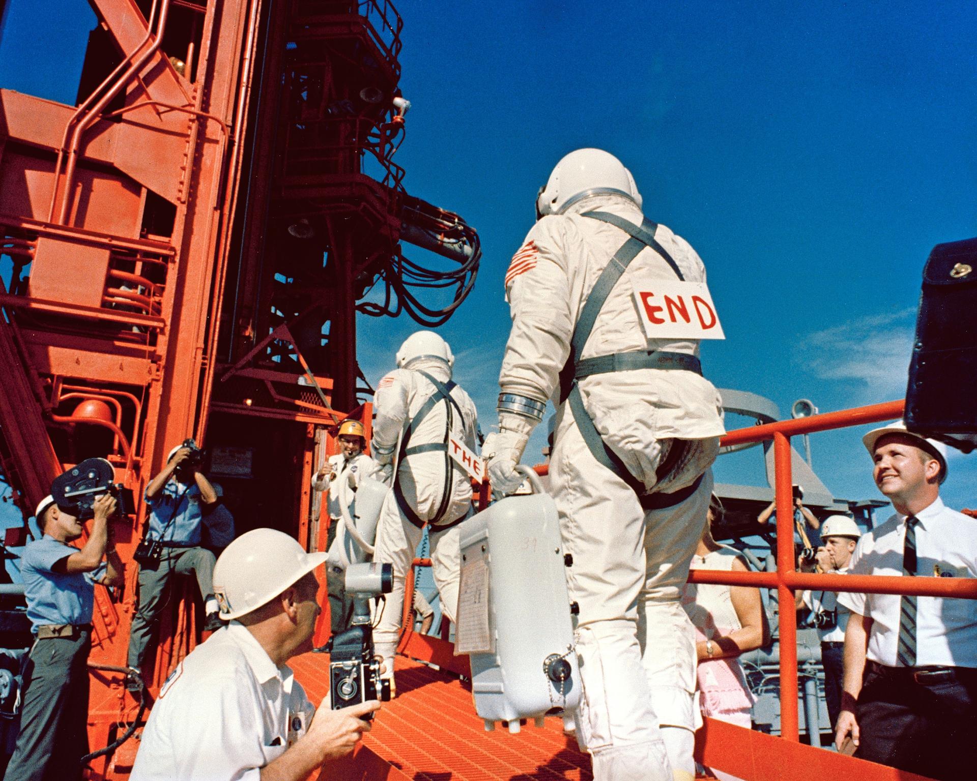 The Gemini 12 astronauts prepare to enter their spacecraft with notes on their backs reading "The" and "End"
