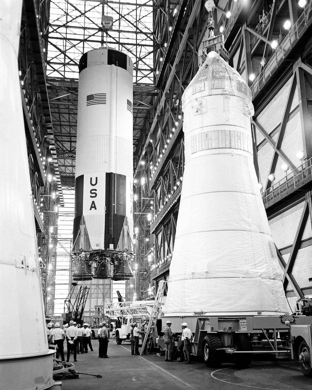 CAPE CANAVERAL, Fla. – The first stage of the Apollo 10 Saturn V space vehicle is hoisted above the transfer aisle in preparation for erection on a mobile launcher within High Bay 2 of the Vehicle Assembly Building. The erection of the 138-foot-long stage marked the first use of mobile launcher 3 and high bay 2. Apollo 10 will be piloted by astronauts Thomas Stafford, John Young and Eugene Cernan. In the foreground are the mated command, service and lunar modules the latter enclosed within the adapter for the Apollo 9 flight of James McDivitt, David Scott and Russel Schweickart. Photo credit: NASA