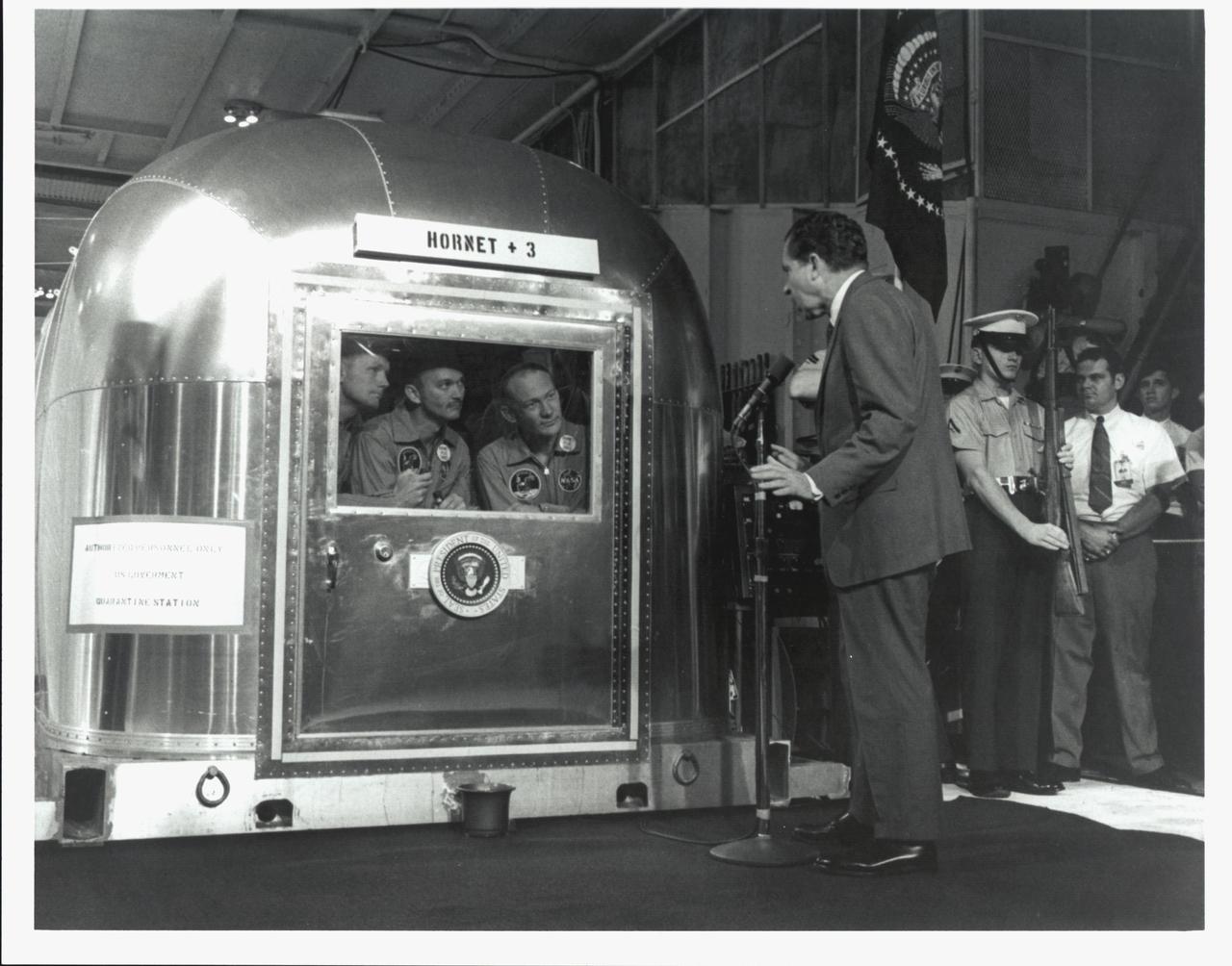 KENNEDY SPACE CENTER, FLA. -  The Apollo 11 astronauts, left to right, Neil A. Armstrong, Michael Collins and Edwin E. Aldrin Jr., inside the Mobile Quarantine Facility aboard the USS Hornet, listen to President Richard M. Nixon as he welcomes them back to Earth and for a job well done.  The astronauts, after their first manned mission to the Moon, splashed down in the Pacific Ocean at 12:50 p.m. EDT about 900 miles southwest of Hawaii.