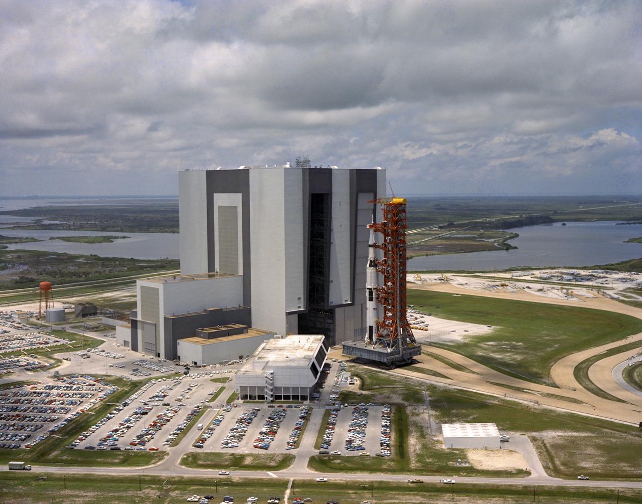 CAPE CANAVERAL, Fla. -- The 363-foot-high Apollo 11 space vehicle towers over the Spaceport’s crawlerway and personnel during its rollout today from the Vehicle Assembly Building’s high bay 1 to Launch Complex 39A.  The transporter carried the vehicle and its mobile launcher along the 3.5-mile-roadway at an average speed of less than one mile per hour, arriving at the launch pad some seven hours after rollout began.  The vehicle is to launch Apollo 11 astronauts Neil A. Armstrong, Michael Colins and Edwin E. Aldrin Jr. on the nation’s first manned lunar landing mission.   Photo credit: NASA