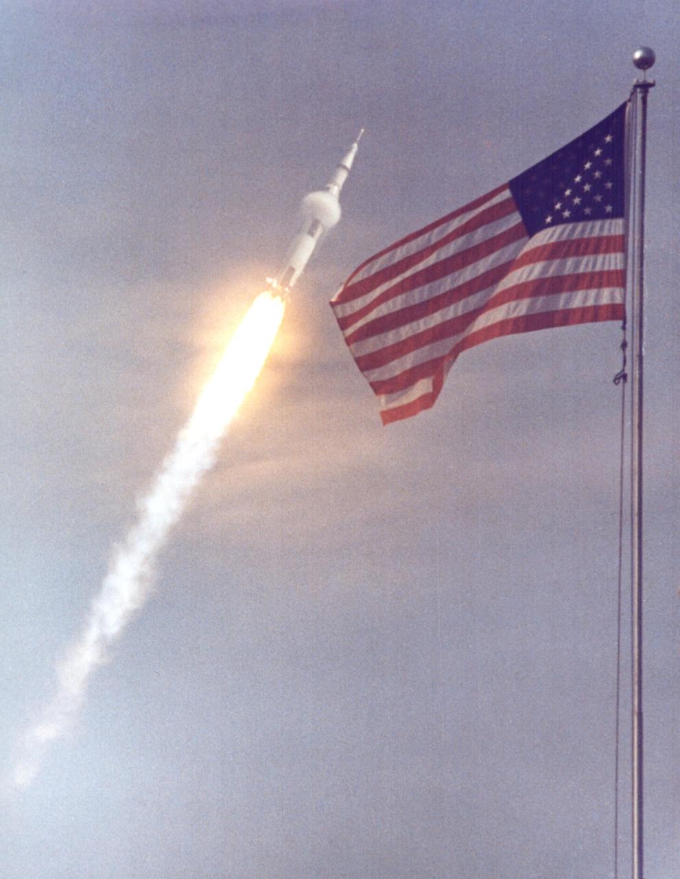 KENNEDY SPACE CENTER, FLA. - The American flag heralds the flight of Apollo 11, man's first lunar landing mission. The Apollo 11 Saturn V space vehicle lifted off with astronauts Neil A. Armstrong, Michael Collins and Edwin E. Aldrin Jr. at 9:32 a.m. EDT from KSC's Launch Complex 39A. During the planned eight-day mission, Armstrong and Aldrin will descend in a Lunar Module (LM) to the Moon's surface while Collins orbits overhead in the Command Module. The two astronauts are to spend 22 hours on the Moon, including two-and-one-half hours outside the LM. They will gather samples of lunar material and will deploy scientific experiments that will transmit data about the lunar environment. They will rejoin Collins in the Command Module for the return trip to Earth.