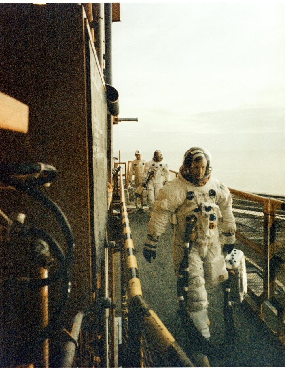 KENNEDY SPACE CENTER, FLA. - Astronauts Neil A. Armstrong (front) and Edwin E. Aldrin Jr. walk across the mobile launcher to enter their Apollo 11 spacecraft. Along with them is Joe Schmidt, a suit technician from Johnson Space Center. Not shown is the third member of the crew, astronaut Michael Collins. Liftoff of Apollo 11 is scheduled at 9:32 a.m. EDT from Pad 39A, which will begin man's first lunar landing mission.