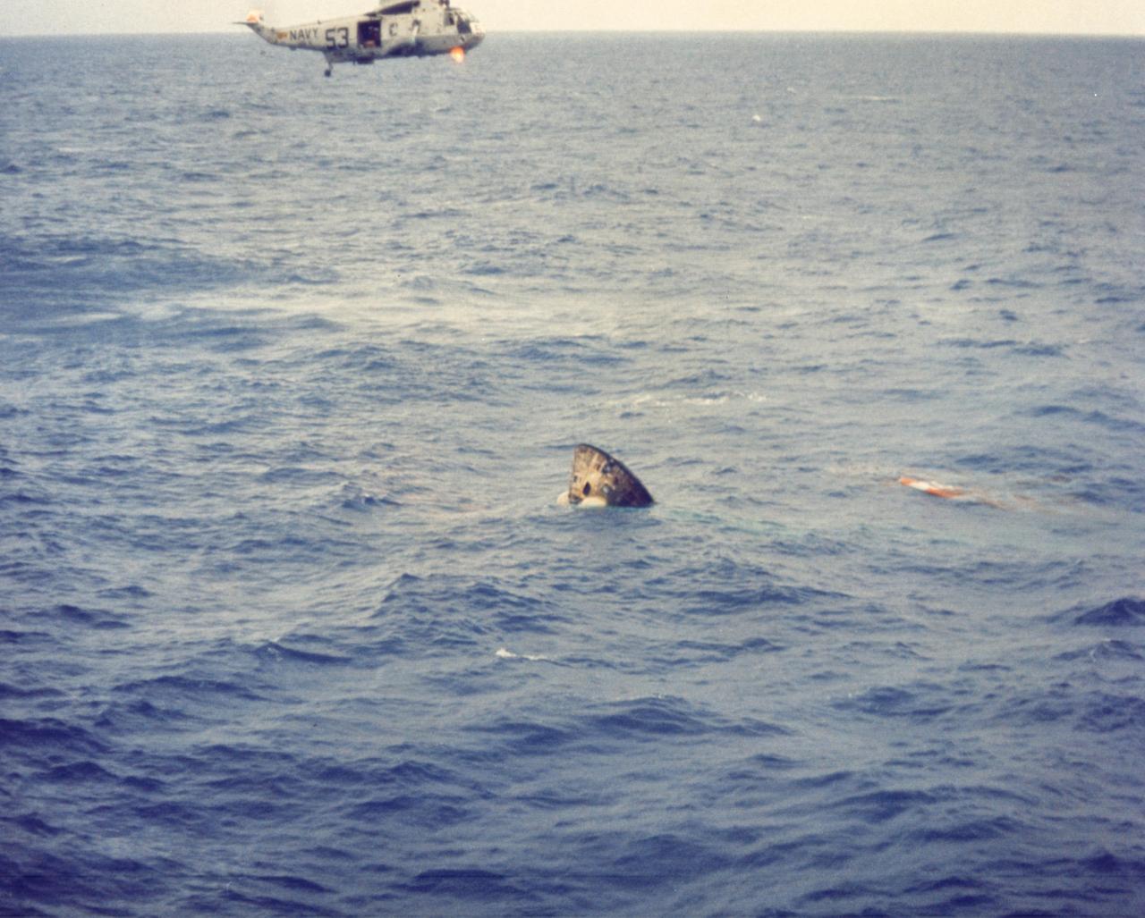 JOHNSON SPACE CENTER, HOUSTON, TEXAS -  A recovery helicopter hovers above the Apollo 11 spacecraft seconds after it splashed down in the Pacific Ocean July 24, 1969, at 12:50 p.m. EDT 900 miles southwest of Hawaii.   The spacecraft turned apex down after impact, as shown here, but inflatable bags repositioned it shortly after this view was taken.