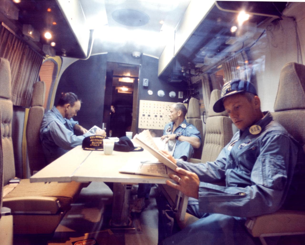 KENNEDY SPACE CENTER, FLA. - Within the Mobile Quarantine Facility, Apollo 11 astronauts (left to right) Michael Collins, Edwin E. Aldrin Jr. and Neil A. Armstrong relax following their successful lunar landing mission. They spent two-and-one-half days in the quarantine trailer enroute from the USS Hornet, prime recovery ship, to the Lunar Receiving Laboratory at the Manned Spacecraft Center in Houston. The Hornet docked at Pearl Harbor where the trailer was transferred to a jet aircraft for the flight to Houston.