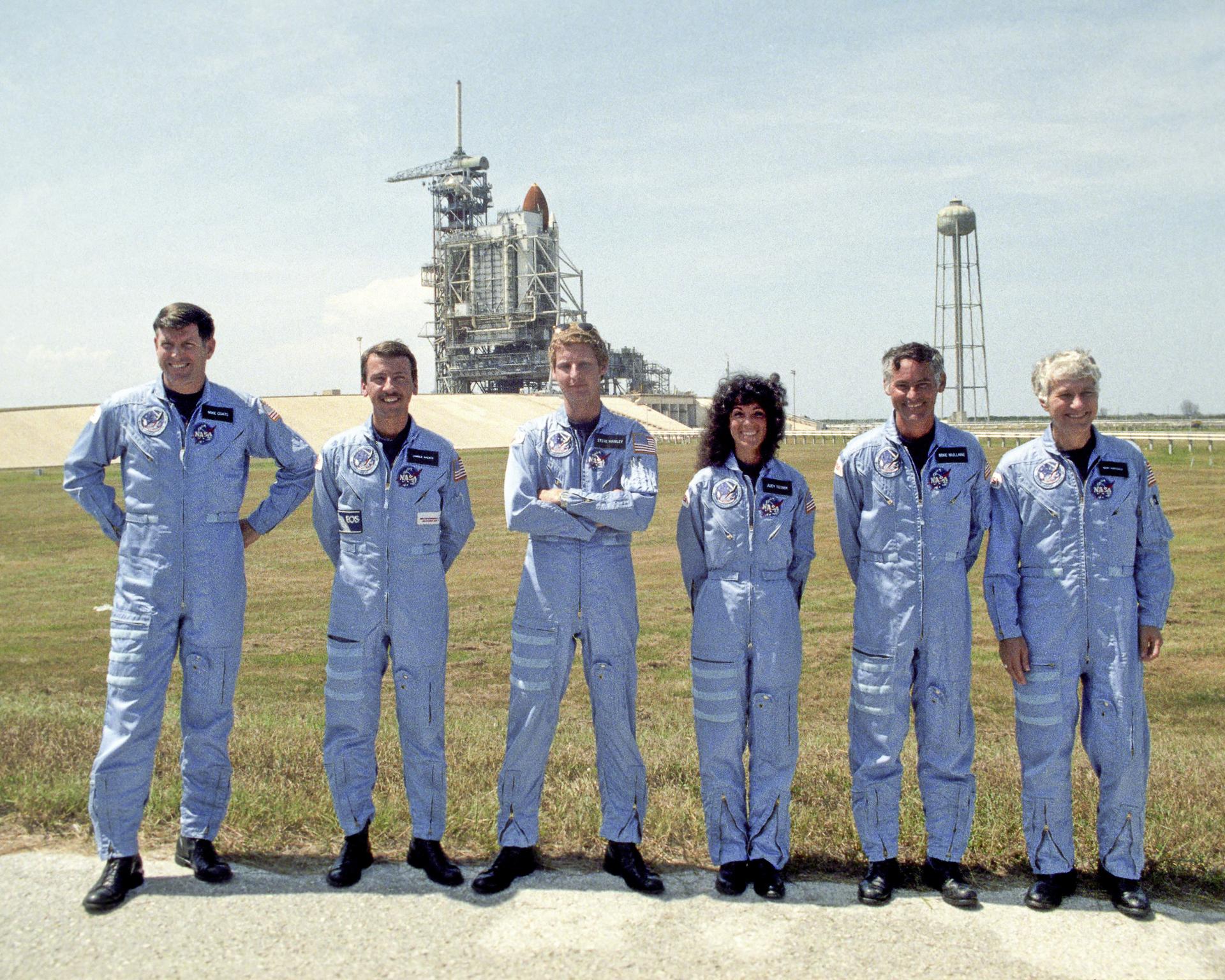 Crew photo of STS-41D posed in front of the launchpad with Discovery in the background