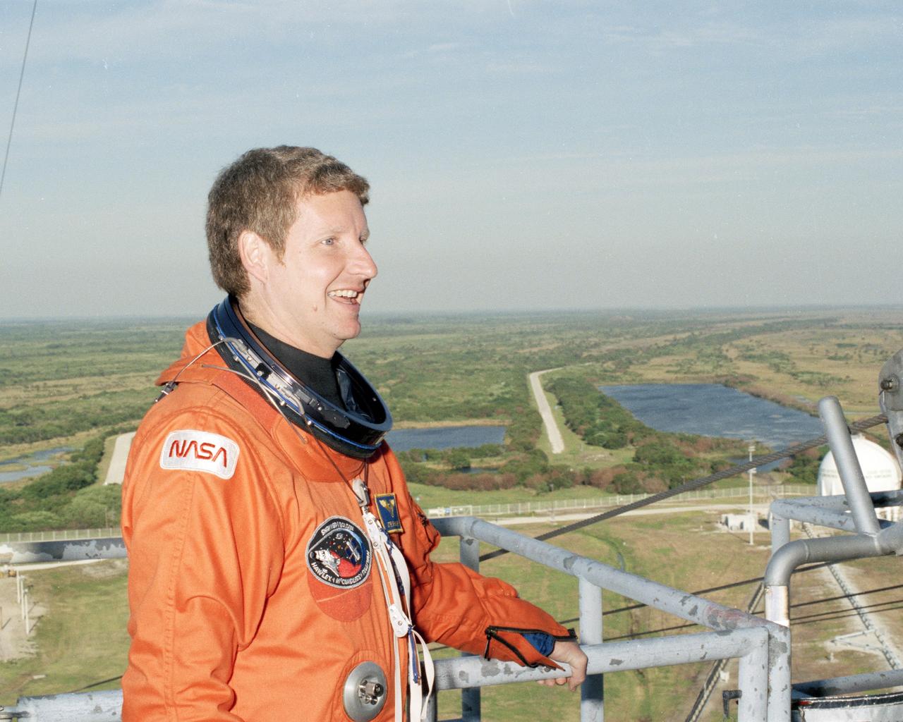 Wide-open Florida terrain creates a dramatic backas STS-31 Mission Specialist Steven A. Hawley stands near the emergency exit system at the 194-foot level of Launch Pad 39B during the Terminal Countdown Demonstration Test, or TCDT. Conducted March 19-20, the TCDT is a dress rehearsal for launch, simulating final countdown from the T-24 hour mark up to T-5 seconds. Space shuttle mission STS-31 is set to lift off on April 12, carrying a five-member crew and the Hubble Space Telescope. Photo credit: NASA