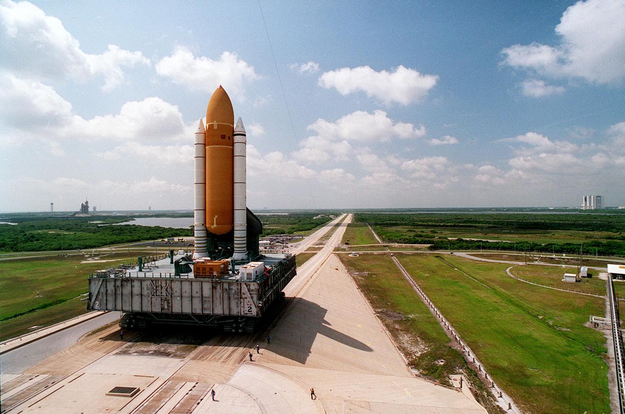 The Space Shuttle Discovery slowly and carefully makes the 4.2- mile (6.8 kilometer) trek from the Vehicle Assembly Building, background at right, to Launch Pad 39B on its Mobile Launcher Platform carried by the Crawler Transporter. Pad 39A, with the Shapce Shuttle Atlantic poised for liftoff, is in background at left. Discovery is scheduled to fly first, on STS-70 targeted for June 8. Atlantis' mission, STS-71, is scheduled no earlier than June 22. 