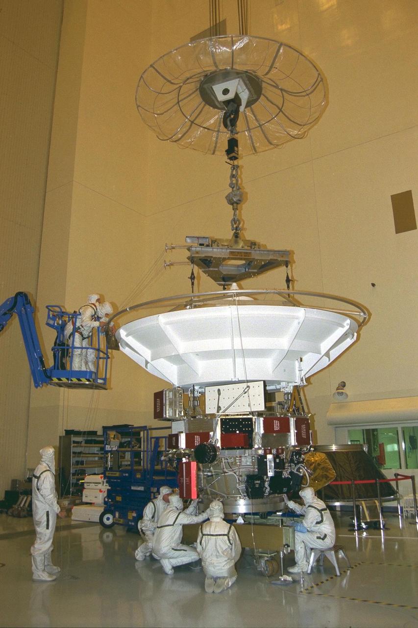 Jet Propulsion Laboratory (JPL) technicians in a blue crane  at the top of the white upper equipment module (UEM) level the UEM prior to separation  from its dolly. The module will be prepared for stacking atop Cassini’s propulsion  module in the Payload Hazardous Servicing Facility at KSC. Cassini, a four-year, close-up study of the Saturnian system, is scheduled for launch from Cape Canaveral Air  Station in October 1997. It will take seven years for the spacecraft to reach Saturn.  Scientific instruments carried aboard the spacecraft will study Saturn’s atmosphere,  magnetic field, rings, and several moons. JPL is managing the Cassini project for NASA
