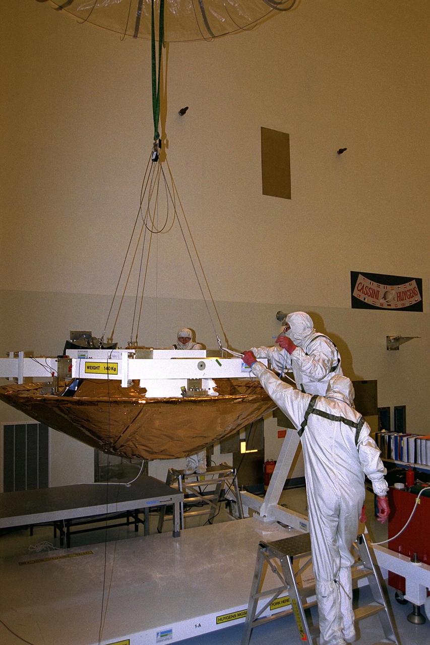 Daimler-Benz Aerospace staff prepare to remove the lift  fixture used to install the back cover on the Huygens probe, the conical structure in the  white workstand, in the Payload Hazardous Servicing Facility at KSC. Instruments  mounted on the probe, which was developed by the European Space Agency (ESA), will  receive atmospheric and surface data on Saturn’s main moon, Titan, to send back to Earth  as part of the Cassini mission. The back cover, yet to be attached to the Cassini orbiter,  will protect the probe during descent onto Titan. A four-year, close-up study of the  Saturnian system, Cassini is scheduled for launch from Cape Canaveral Air Station in  October 1997. It will take seven years for the spacecraft to reach Saturn. Aerospatiale is  the prime contractor for ESA