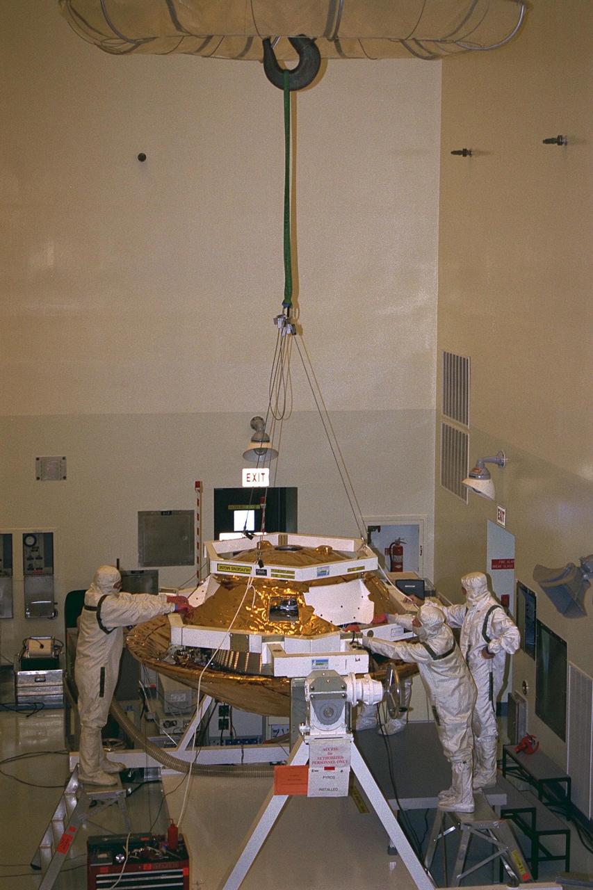 Daimler-Benz Aerospace staff install the back cover on the  Huygens probe in the Payload Hazardous Servicing Facility at KSC in July. Instruments  mounted on the probe, which was developed by the European Space Agency (ESA), will  receive atmospheric and surface data on Saturn’s main moon, Titan, to send back to Earth  as part of the Cassini mission. The back cover, yet to be attached to the Cassini orbiter,  will protect the probe during descent onto Titan. A four-year, close-up study of the  Saturnian system, the mission is scheduled for launch from Cape Canaveral Air Station in  October 1997. It will take seven years for the spacecraft to reach Saturn. Aerospatiale is  the prime contractor for ESA