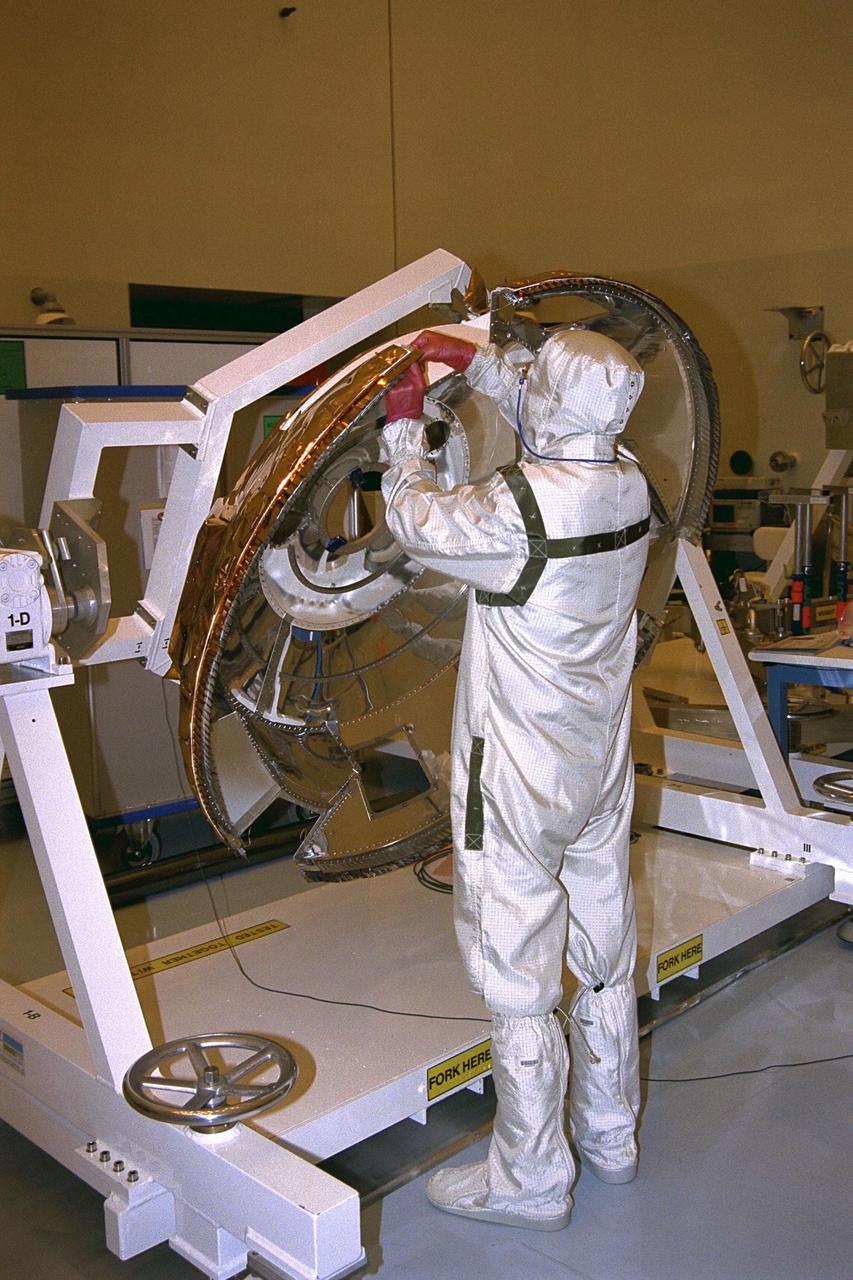A Daimler-Benz Aerospace staff member installs thermal  blanket insulation on the back cover of the Huygens probe in the Payload Hazardous  Servicing Facility at KSC in July. Instruments mounted on the probe, which is owned by  the European Space Agency (ESA), will receive atmospheric and surface data on Saturn’s  main moon, Titan, to send back to Earth as part of the Cassini mission. The back cover,  yet to be attached to the Cassini orbiter, will protect the probe during descent onto Titan.   A four-year, close-up study of the Saturnian system, the mission is scheduled for launch  from Cape Canaveral Air Station in October 1997. It will take seven years for the  spacecraft to reach Saturn. Aerospatiale is the prime contractor for ESA