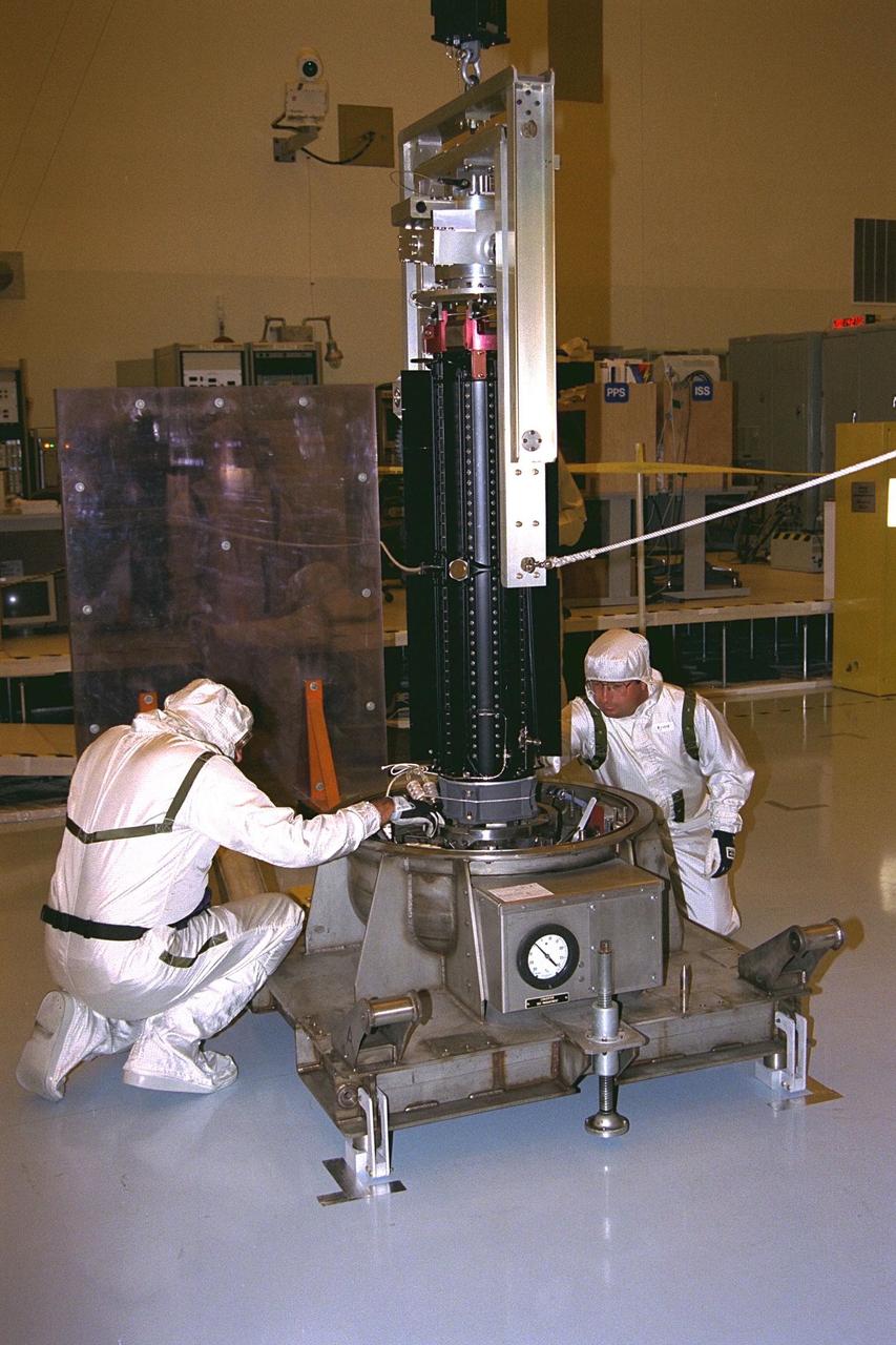 Lockheed Martin Missile and Space Co. employees  Joe Collingwood, at right, and Ken Dickinson retract pins in the storage base to release  a radioisotope thermoelectric generator (RTG) in preparation for hoisting operations.  This RTG and two others will be installed on the Cassini spacecraft for mechanical and  electrical verification testing in the Payload Hazardous Servicing Facility. The RTGs will  provide electrical power to Cassini on its 6.7-year trip to the Saturnian system and  during its four-year mission at Saturn. RTGs use heat from the natural decay of  plutonium to generate electric power. The generators enable spacecraft to operate at  great distances from the Sun where solar power systems are not feasible. The Cassini  mission is targeted for an Oct. 6 launch aboard a Titan IVB/Centaur expendable launch  vehicle. Cassini is built and managed by NASA’s Jet Propulsion Laboratory