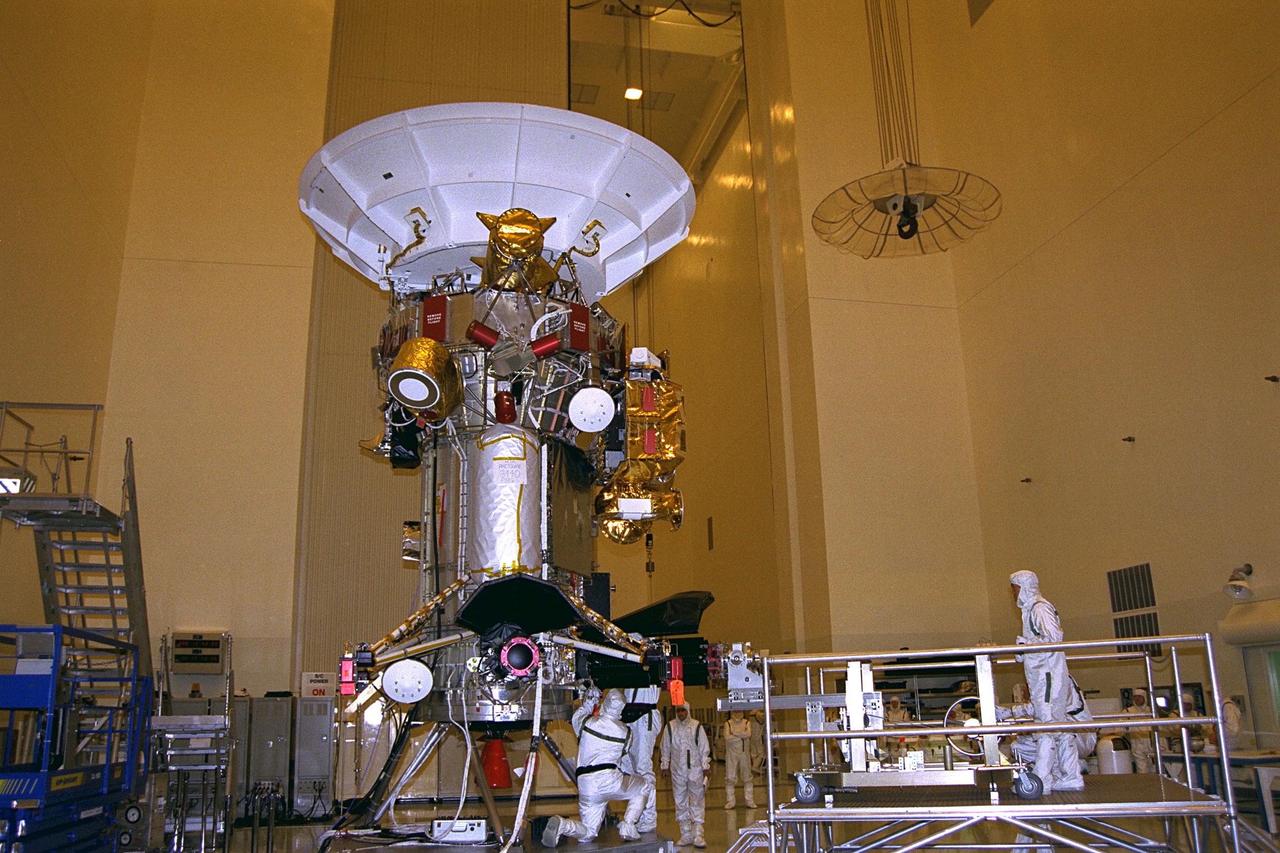 Jet Propulsion Laboratory (JPL) employees bolt a  radioisotope thermoelectric generator (RTG) onto the Cassini spacecraft, at left, while  other JPL workers, at right, operate the installation cart on a raised platform in the  Payload Hazardous Servicing Facility (PHSF). Cassini will be outfitted with three RTGs.  The power units are undergoing mechanical and electrical verification tests in the PHSF.  The RTGs will provide electrical power to Cassini on its 6.7-year trip to the Saturnian  system and during its four-year mission at Saturn. RTGs use heat from the natural  decay of plutonium to generate electric power. The generators enable spacecraft to  operate at great distances from the Sun where solar power systems are not feasible.  The Cassini mission is targeted for an Oct. 6 launch aboard a Titan IVB/Centaur  expendable launch vehicle. Cassini is built and managed by JPL