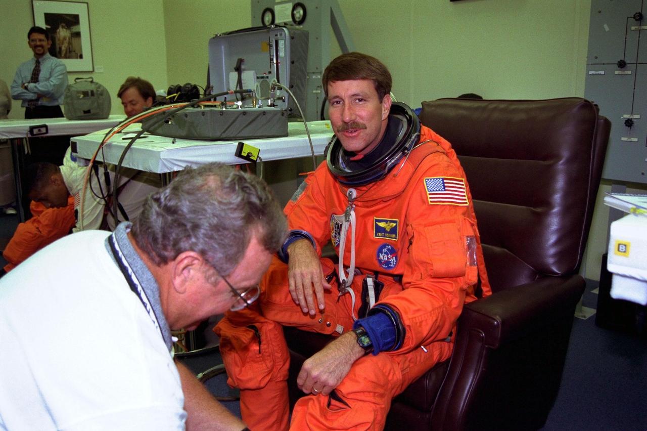 STS-85 Pilot Kent V. Rominger is assisted with his ascent/reentry flight suit in the Operations and Checkout (O&C) Building. He is a commander in the Navy and is on his third Shuttle mission. Rominger previously flew in this capacity on STS-73 and STS-80. He holds a master’s degree in aeronautical engineering and has more than 4,500 hours of flight time and 685 carrier landings. Rominger will assist Commander Curtis L. Brown, Jr. with all phases of the space flight and during the test of International Space Station rendezvous procedures during the Cryogenic Infrared Spectrometers and Telescopes for the Atmosphere-Shuttle Pallet Satellite-2 (CRISTA-SPAS-2) free-flyer retrieval. He will also be busy with the many and varied tasks associated with monitoring and maintaining the orbiter. In addition, Rominger will operate the Solid Surface Combustion Middeck Experiment. The primary payload aboard the Space Shuttle orbiter Discovery is the CRISTA-SPAS-2. Other payloads on the 11-day mission include the Manipulator Flight Demonstration (MFD), and Technology Applications and Science-1 (TAS-1) and International Extreme Ultraviolet Hitchhiker-2 (IEH-2) experiments