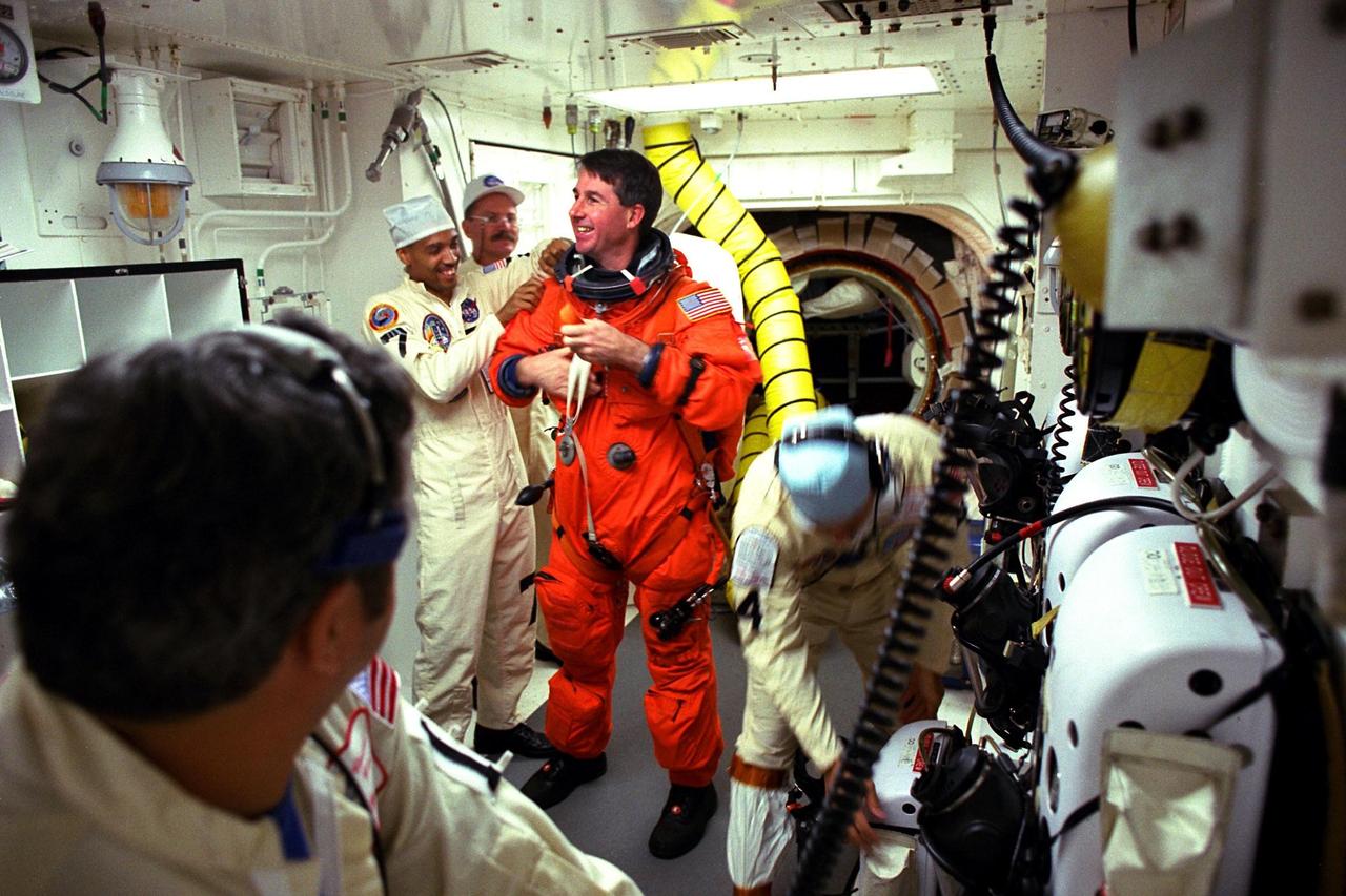 STS-85 Mission Specialist Stephen K. Robinson visits with white room closeout crew members Mike Mangione (left foreground), Carlos Gillis, Jack Burritt (center), and Chris Meinert at Launch Pad 39A as they assist him with his ascent/reentry flight suit before he enters the crew cabin of the Space Shuttle orbiter Discovery