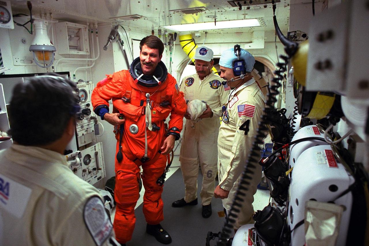 STS-85 Pilot Kent V. Rominger visits with white room closeout crew members Mike Mangione (left foreground), Jack Burritt (center), and Chris Meinert at Launch Pad 39A as they assist him with his ascent/reentry flight suit before he enters the crew cabin of the Space Shuttle orbiter Discovery