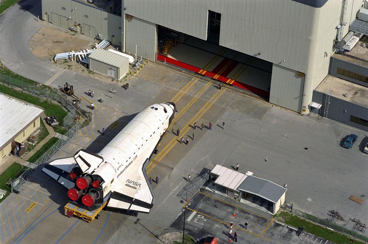Carried atop an orbiter transporter, the Space Shuttle orbiter Atlantis rolls out of Orbiter Processing Facility Bay 3, in background, en route to the Vehicle Assembly Building (VAB). This photo was taken from the roof of the VAB. The "rollover" of the orbiter is one of the prelaunch milestones. Atlantis is being readied for the next mission, STS-86, which is targeted for a September launch. STS-86 will be the seventh of nine planned dockings of the Space Shuttle orbiter with the Russian Space Station Mir