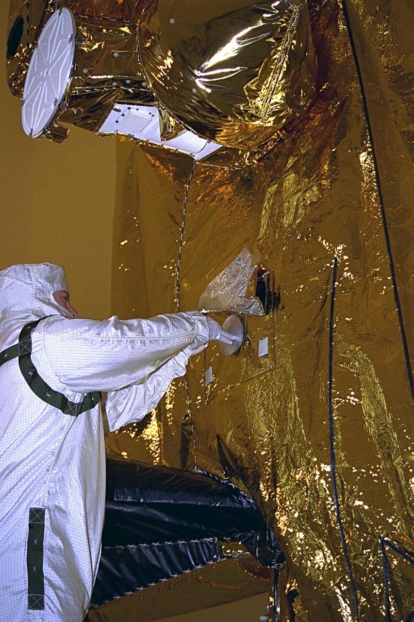 In the Payload Hazardous Servicing Facility (PHSF), Dan Maynard, a Jet Propulsion Laboratory technician, inserts the Digital Video Disk (DVD) into a shallow cavity between two pieces of aluminum that will protect it from micrometeoroid impacts. The package will be mounted to the side of the two-story-tall spacecraft beneath a pallet carrying cameras and other space instruments that will be used to study the Saturnian system. A specially designed, multicolored patch of thermal blanket material will be installed over the disk package. Along with the spacecraft, the disk will reside in Saturn's orbit centuries after the primary mission is completed in July 2008. The Cassini mission is managed for NASA's Office of Space Science, Washington, D.C., by the Jet Propulsion Laboratory, a division of the California Institute of Technology